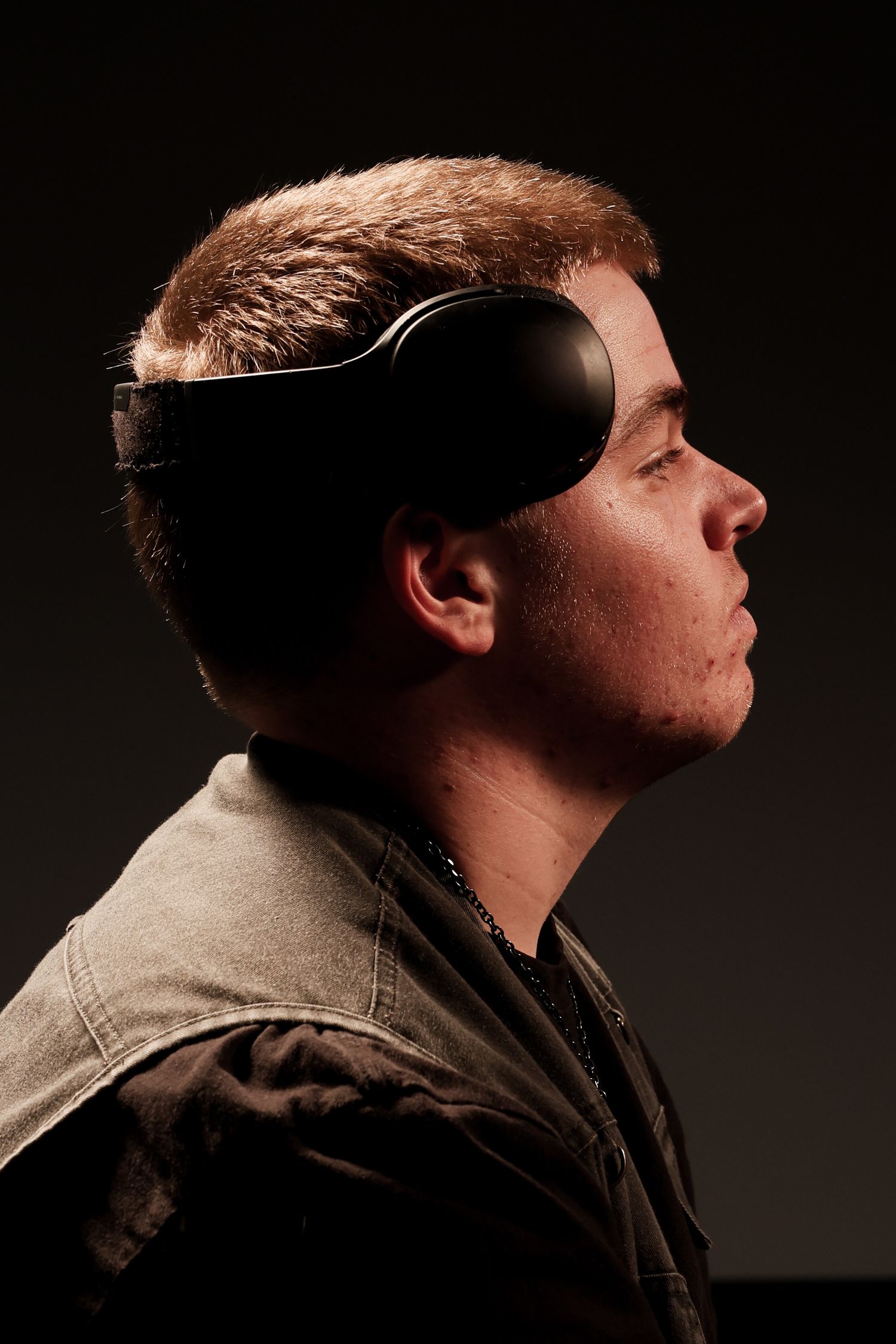 Young man wearing a black VR headset shown in dramatic side profile against dark background.