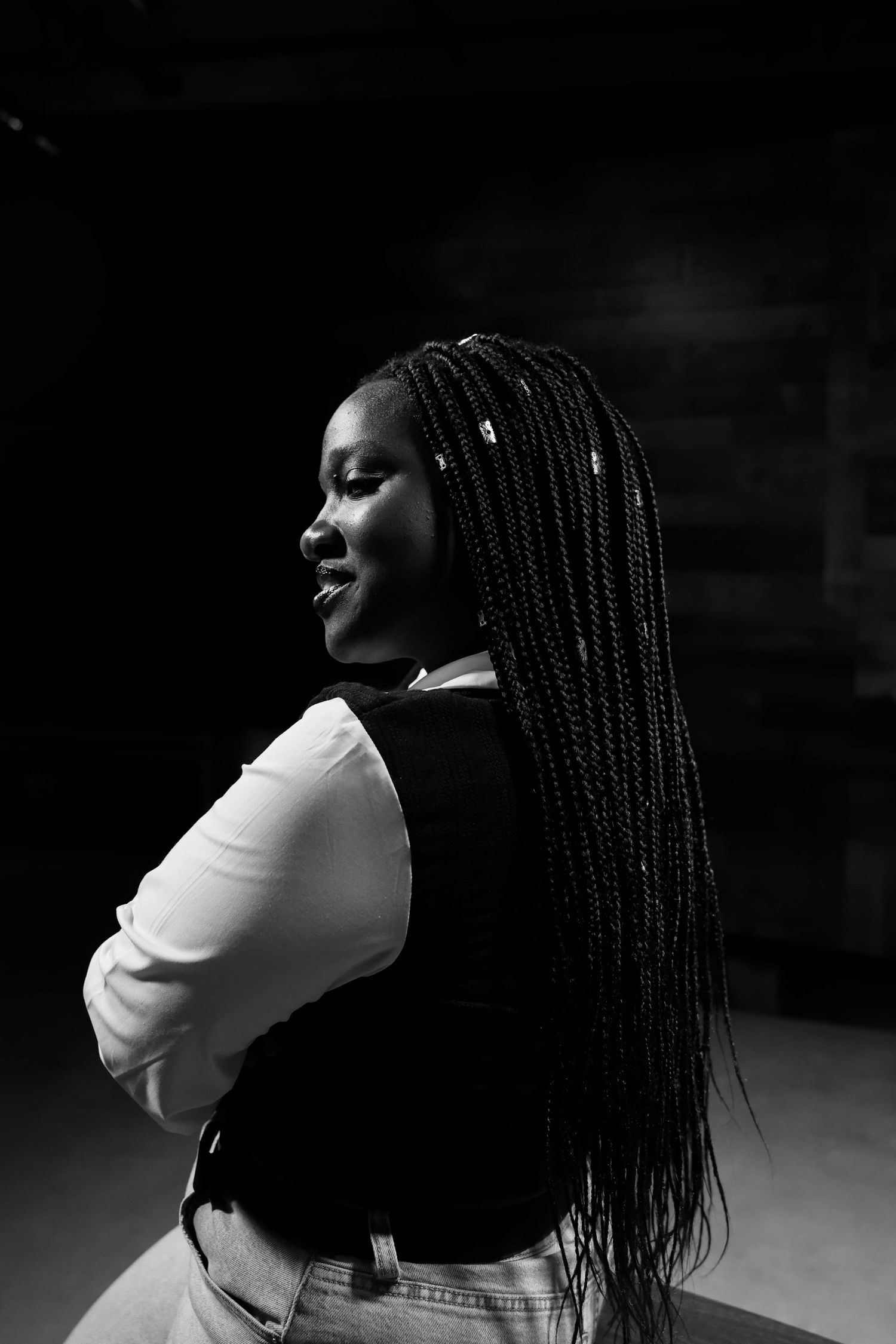 Black and white portrait of a woman with long box braids, arms crossed, looking over her shoulder.