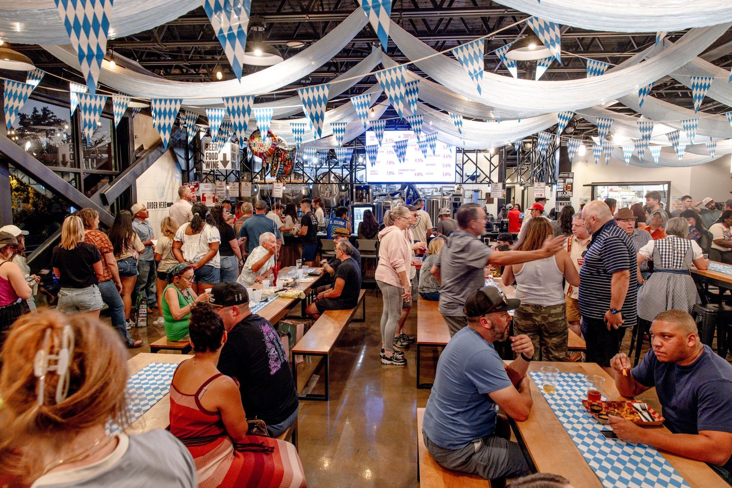 Crowded indoor Oktoberfest celebration with blue and white decorations and long communal tables.