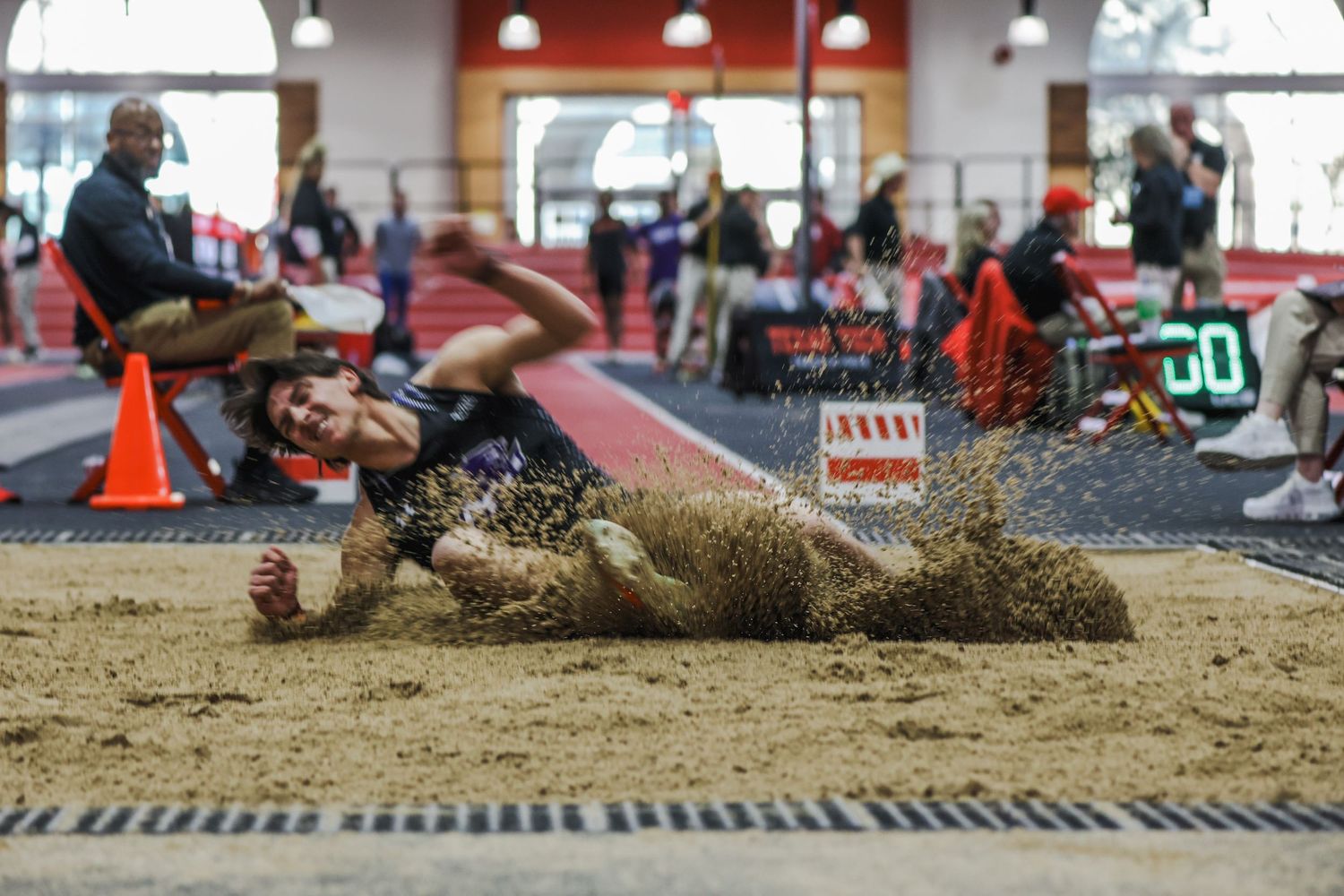 Athlete lands in sand pit during indoor long jump competition.