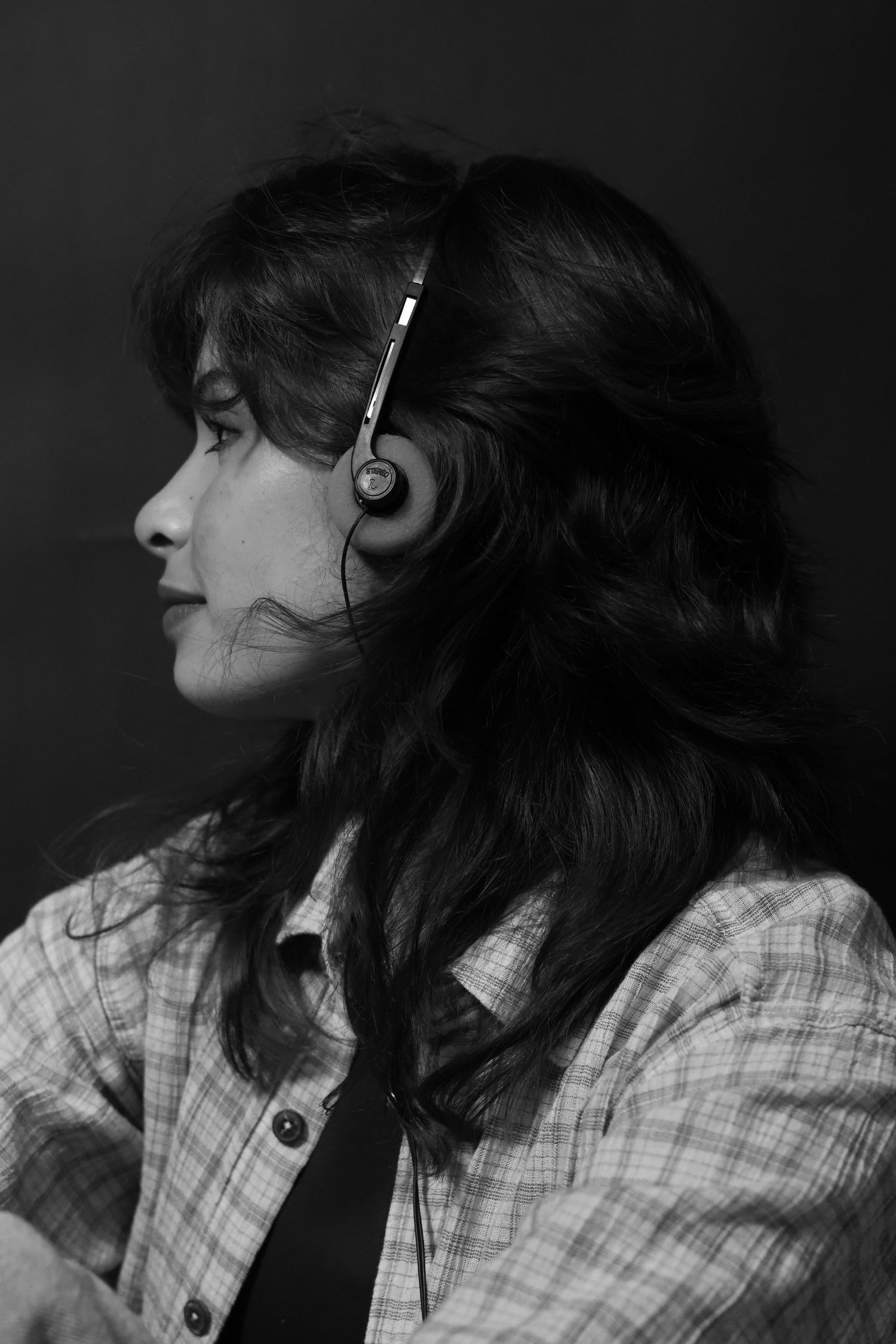 Black and white profile portrait of dark-haired woman wearing headphones and plaid shirt.