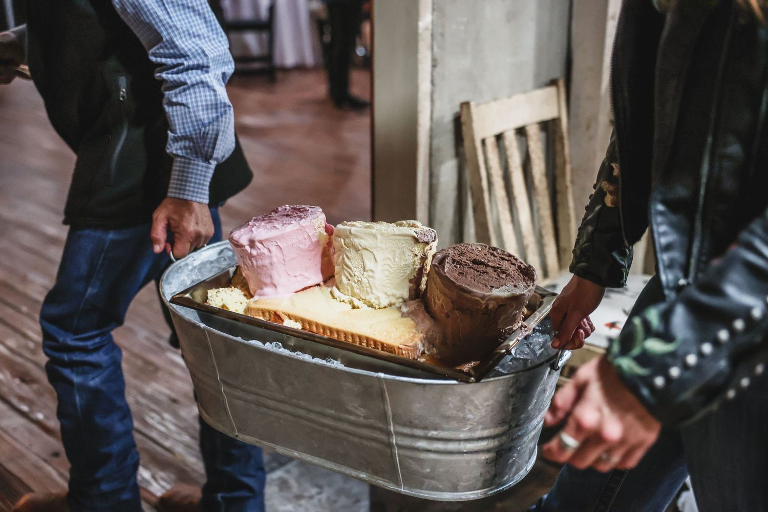Person carrying a galvanized tub filled with assorted colorful cheese blocks at an outdoor food event.