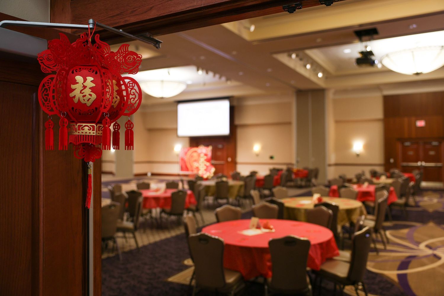 Elegant Chinese New Year banquet hall decorated with red lanterns, round tables, and festive decorations.