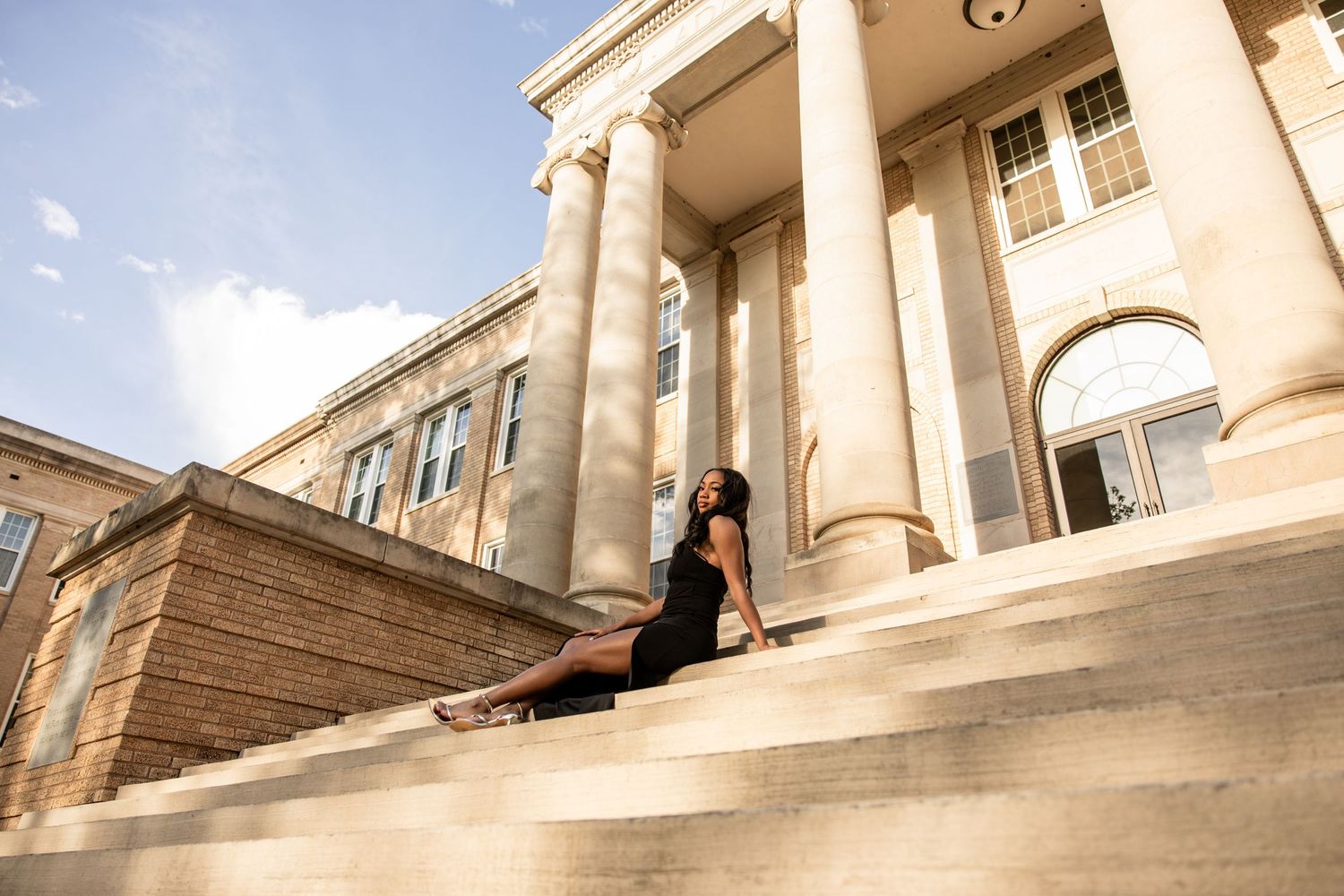 Elegant woman in black dress sitting on steps of grand neoclassical building outdoors.