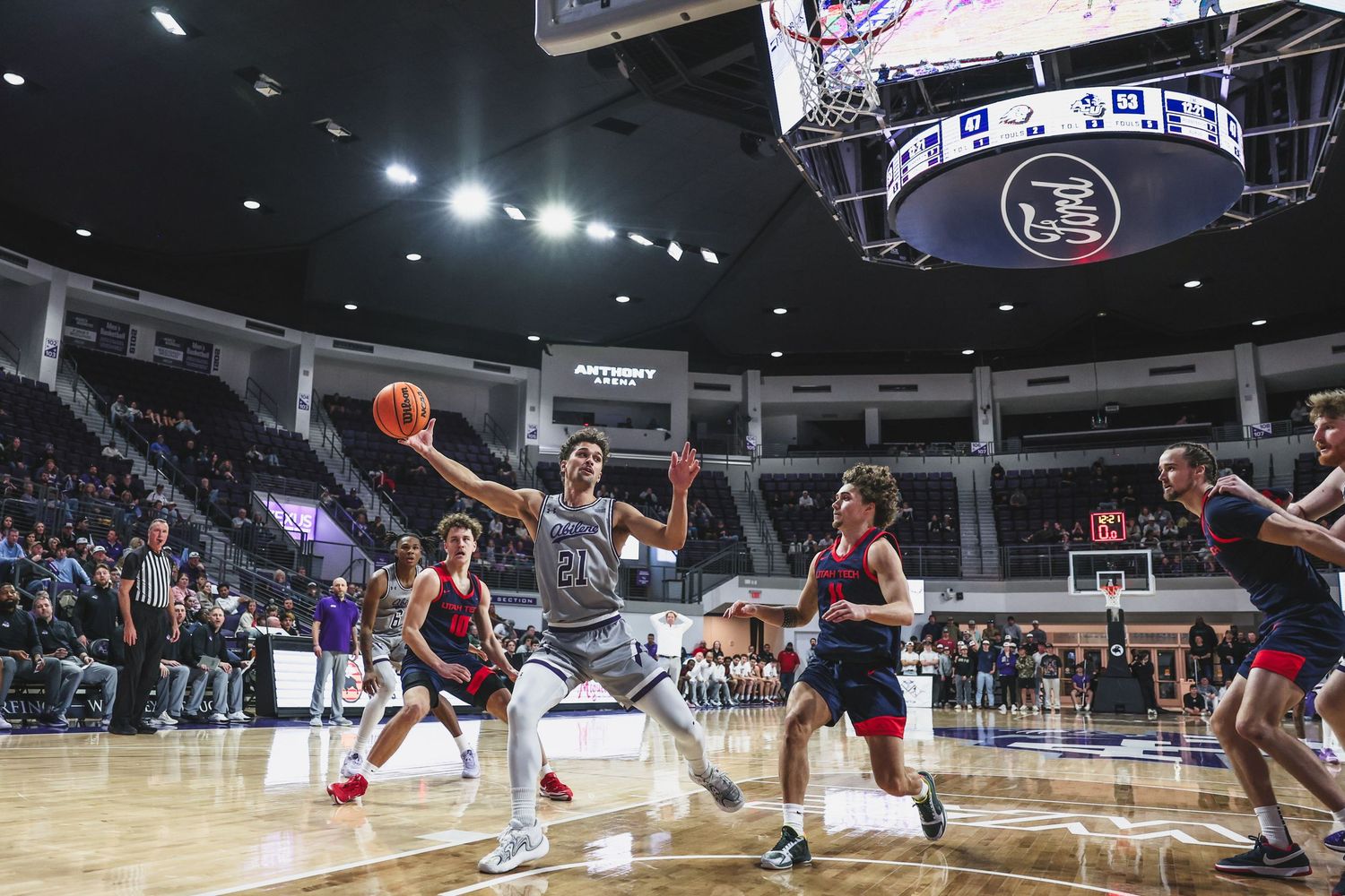 Abilene Christian basketball player drives to the basket during a college game at a packed indoor arena.