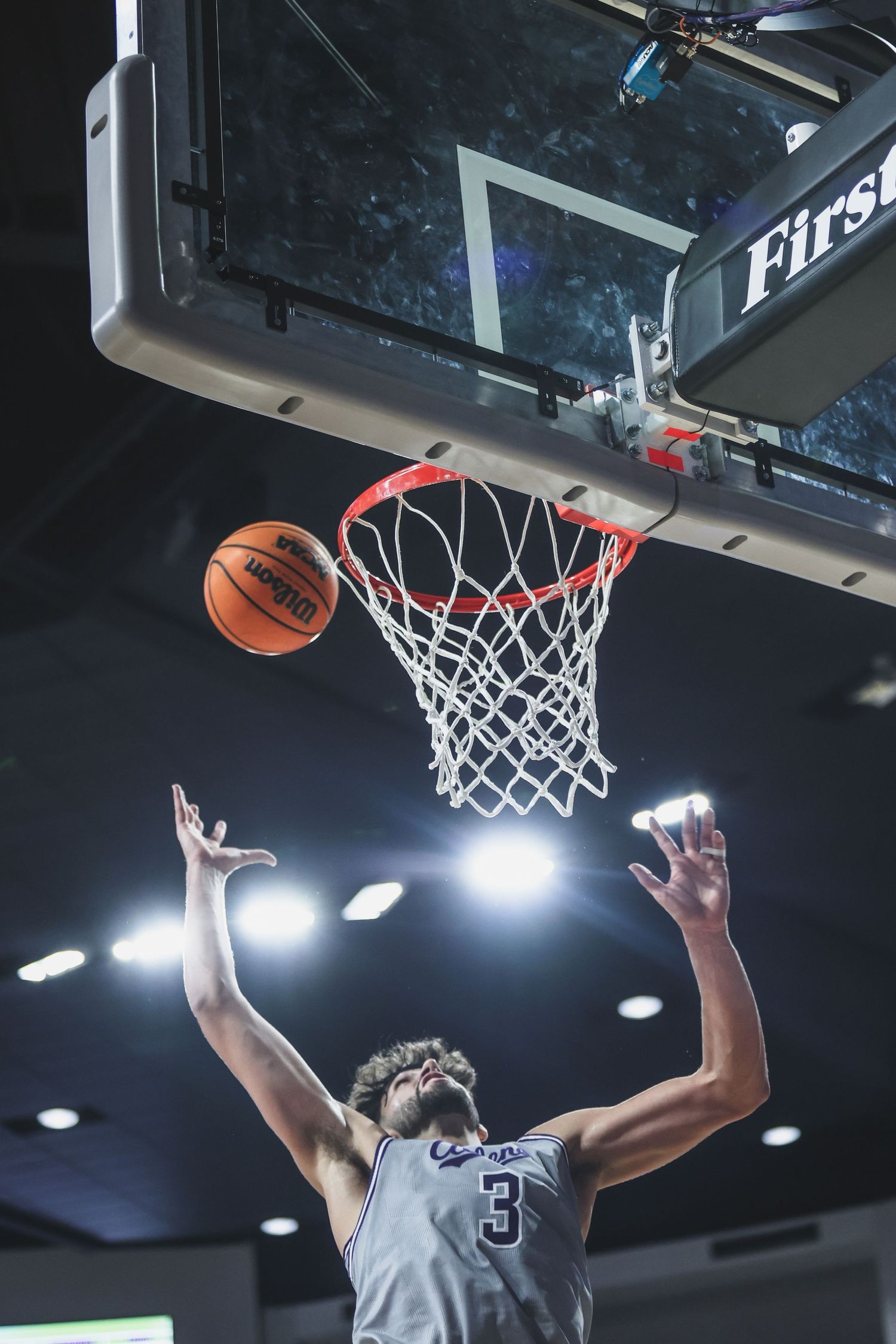 College basketball player #3 in white uniform attempts a layup at the basket during a game.