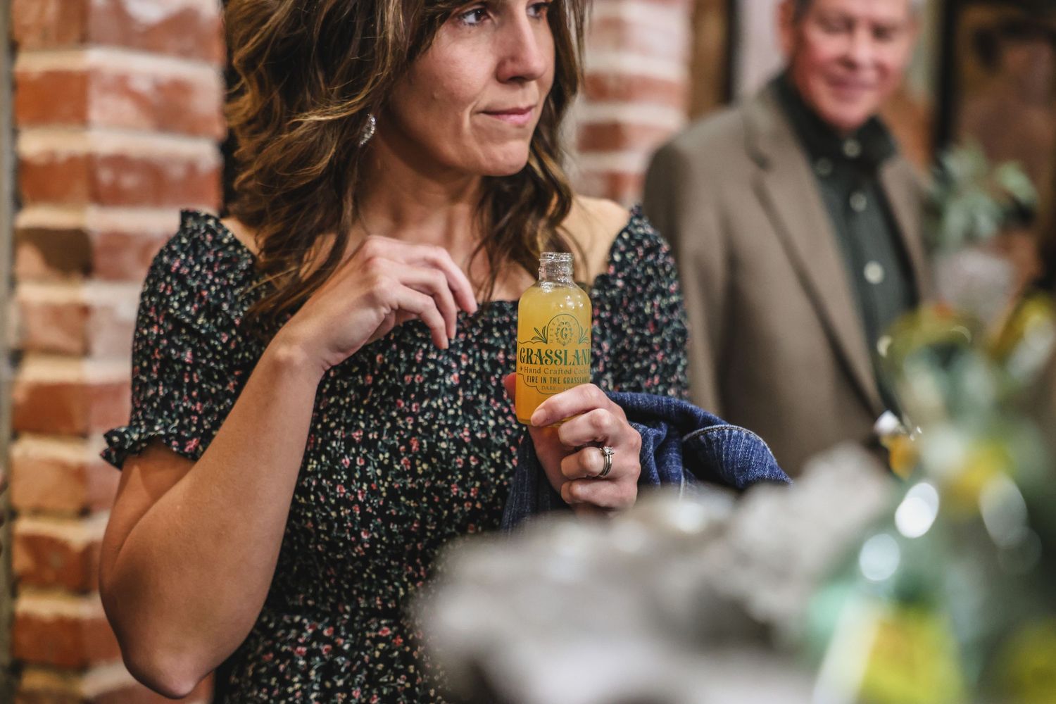 Woman in floral dress sipping a craft cocktail at an indoor event near brick wall.