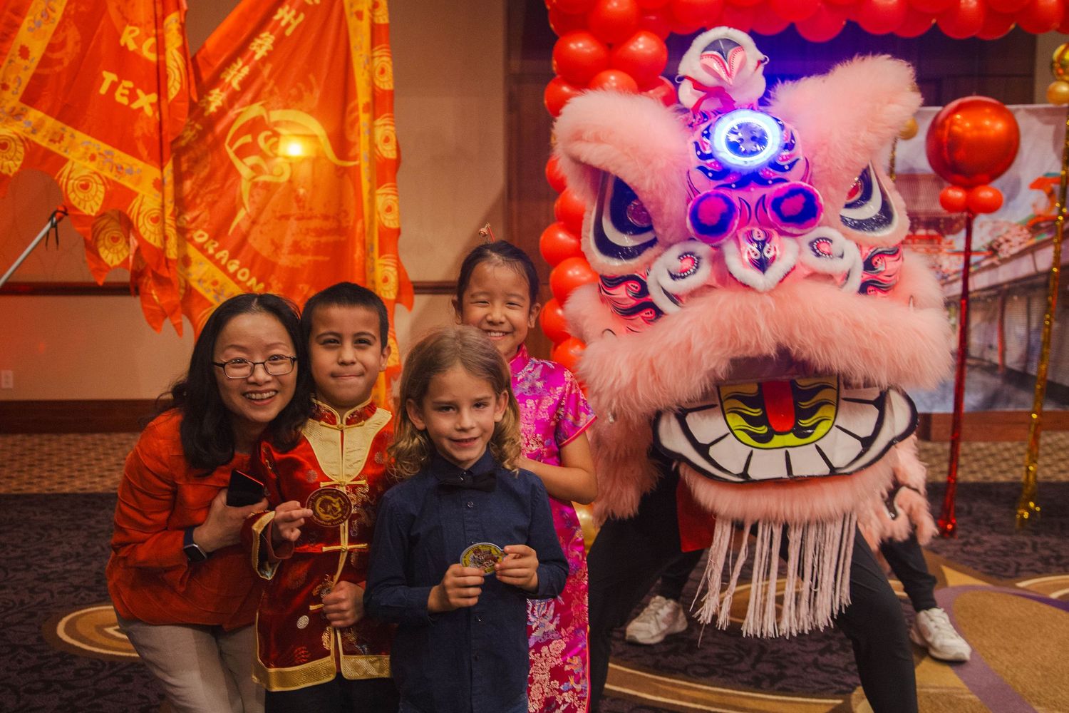 Children and adults pose joyfully with a colorful Chinese lion dance costume at a New Year celebration.