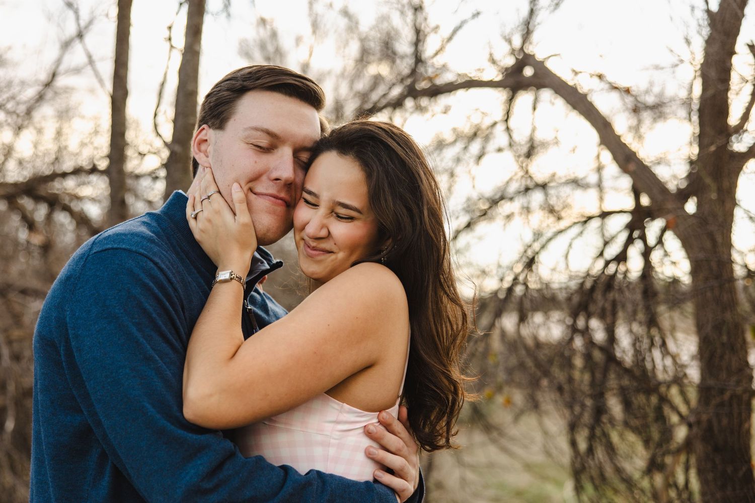 Young couple embracing warmly outdoors among bare trees in golden hour light.