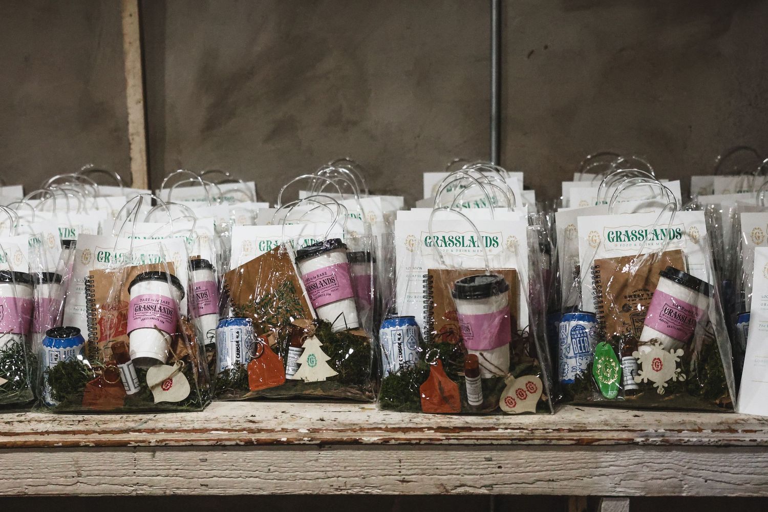 Grasslands branded gift bags with assorted products lined up on wooden shelf display.