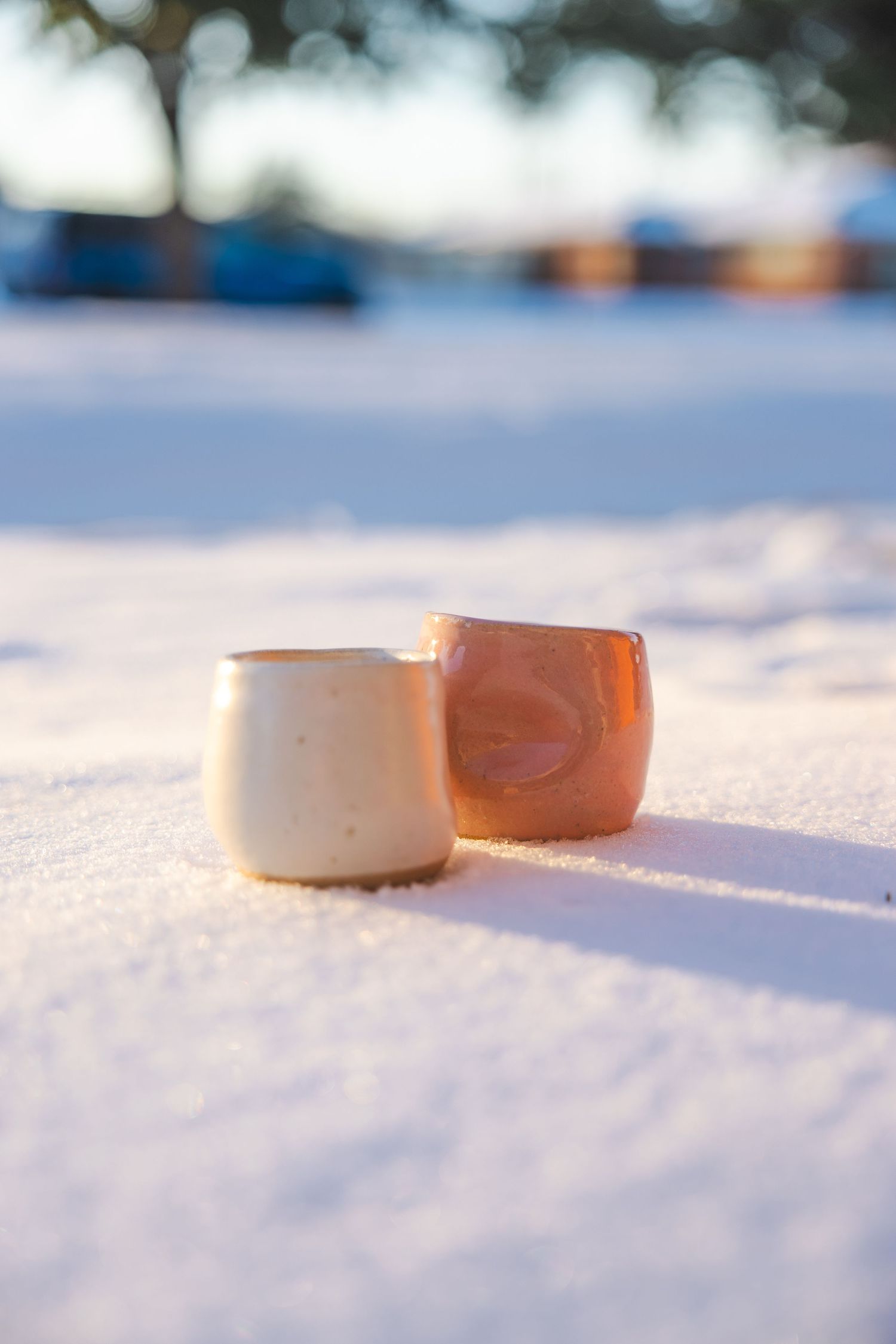 Two handcrafted pottery cups in cream and copper glaze sitting in snow.
