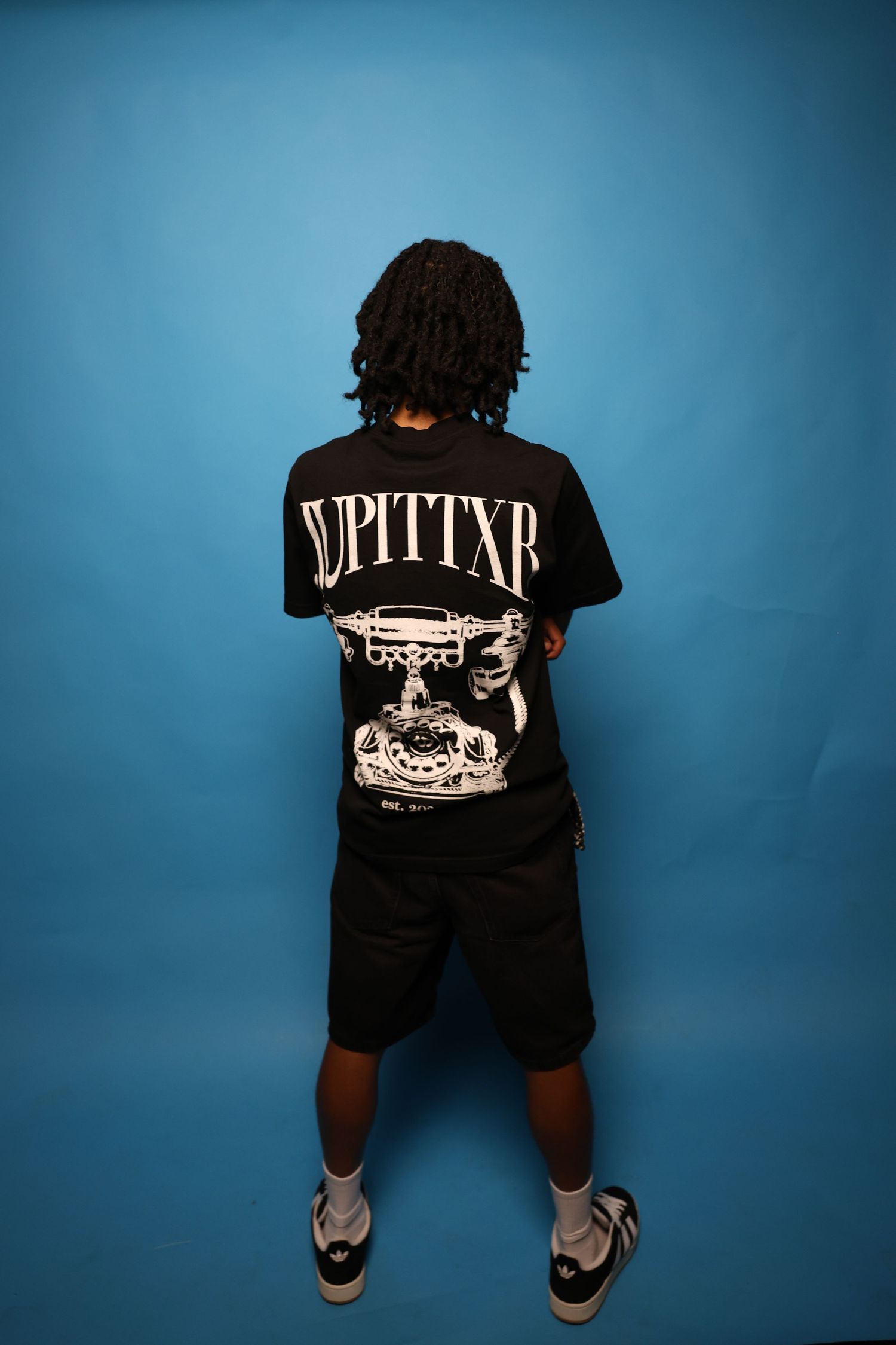 Person standing with back to camera wearing black JUPITTXR graphic tee and shorts.