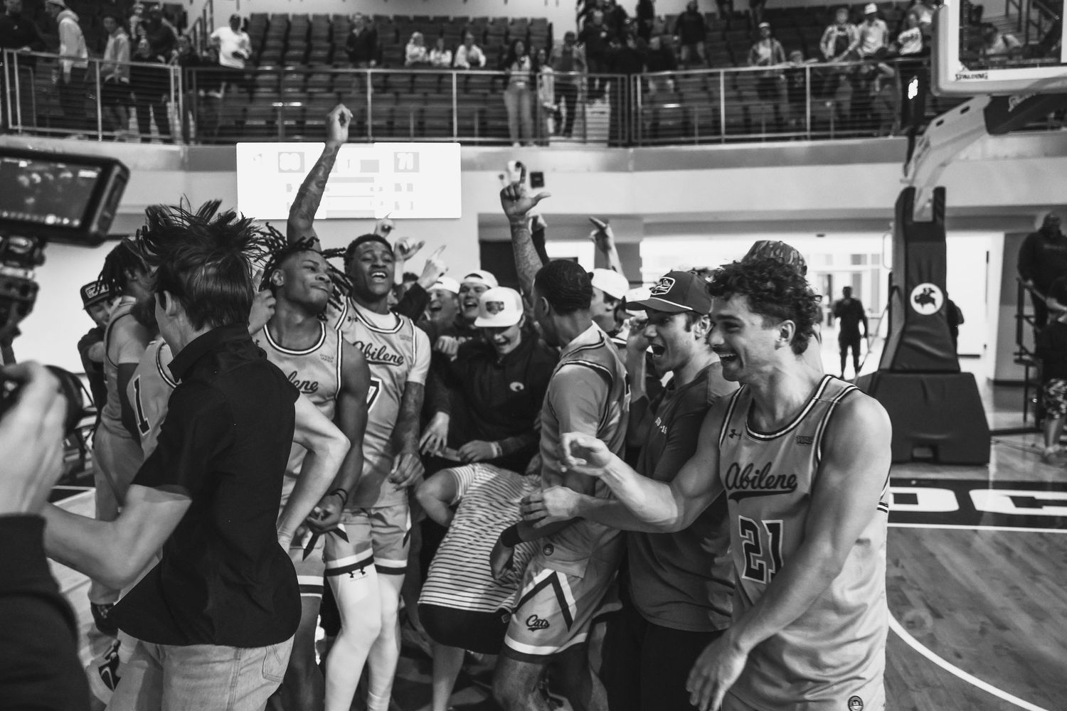College basketball team celebrates victory together on the court in a black and white photo.