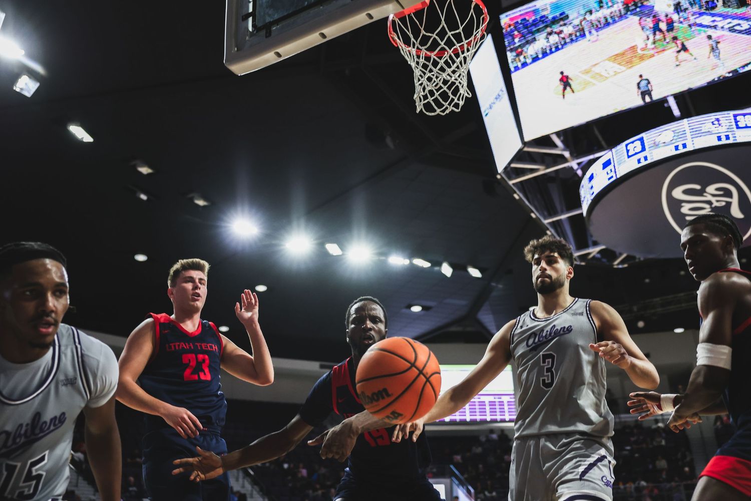 College basketball players battle for a rebound under the basket during an intense indoor arena game.