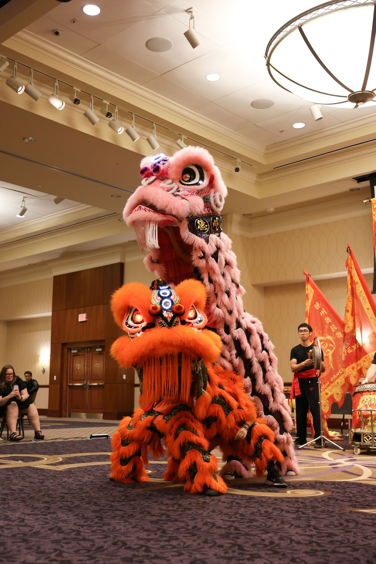 Pink and orange Chinese lion dance costumes perform in a ballroom during a traditional Lunar New Year celebration.