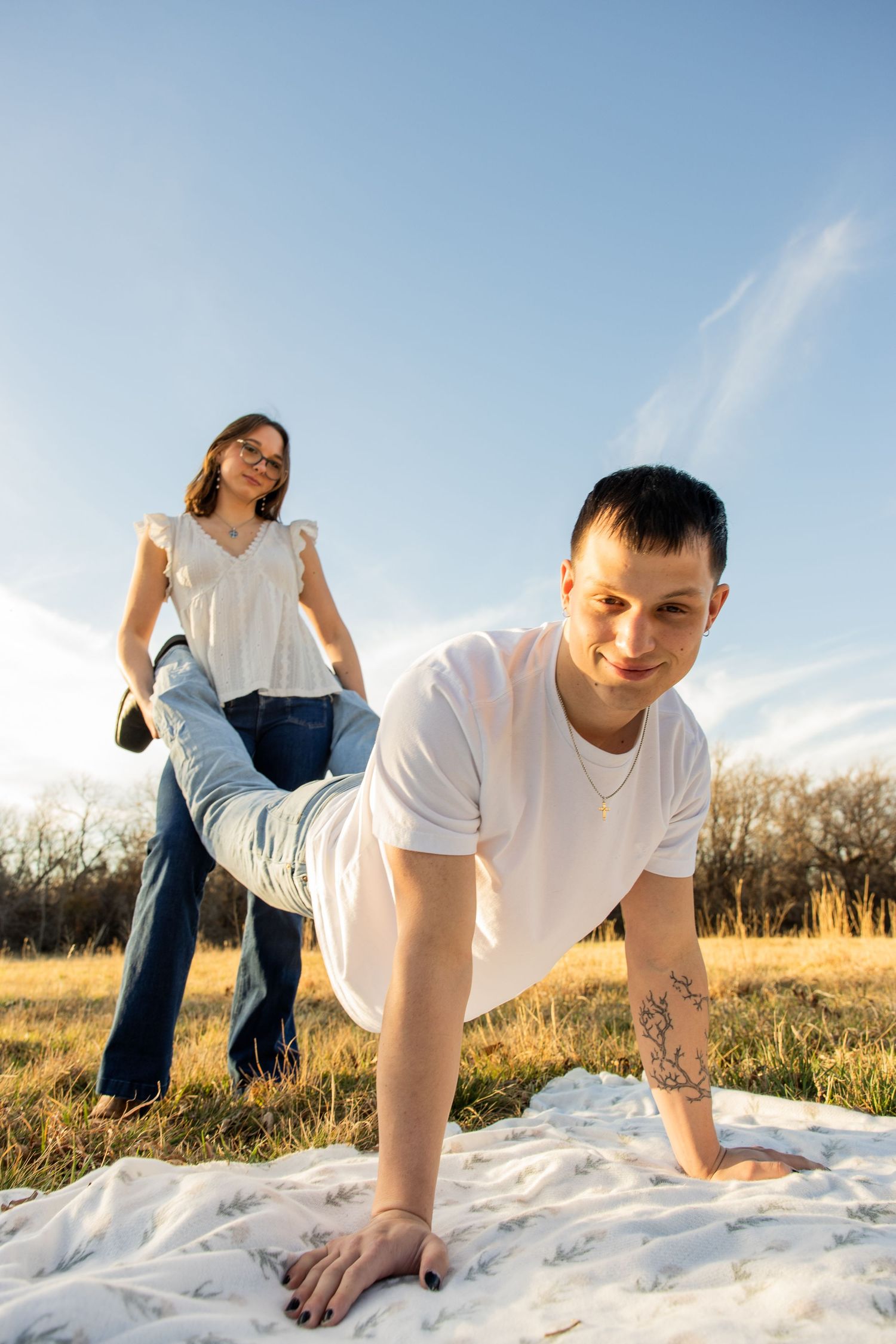 Young couple playing outdoors on a white blanket in a sunny field under blue sky.