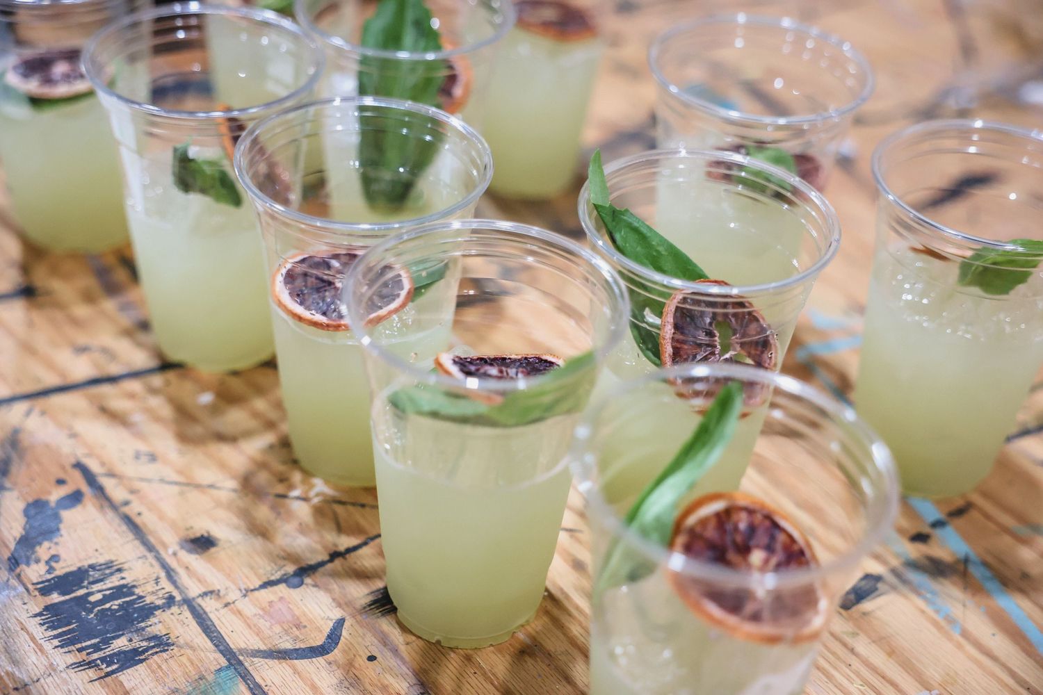 Rows of refreshing green citrus cocktails garnished with basil and dried blood orange slices on a wooden surface.