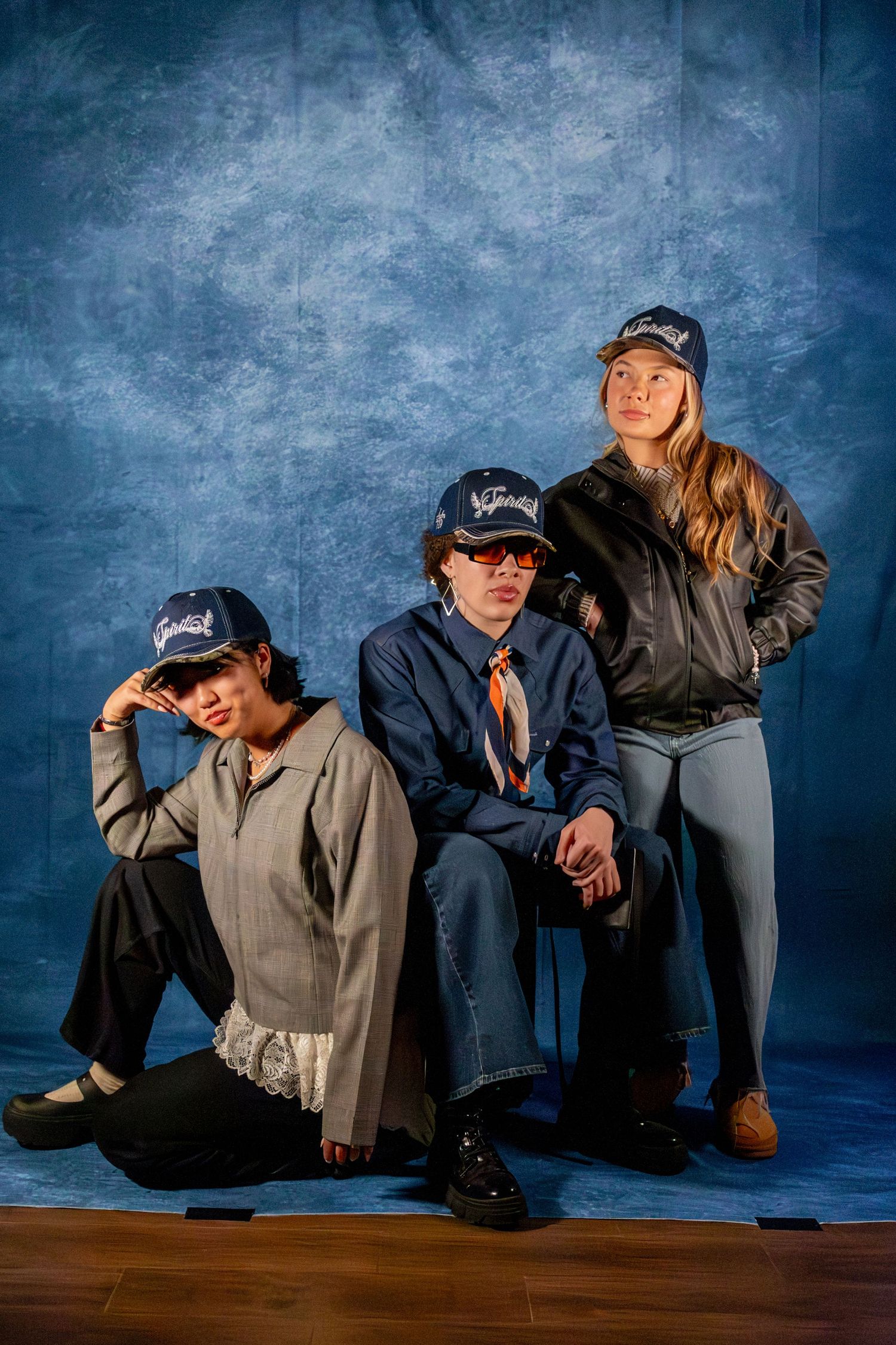 Three models wearing matching navy caps pose together against a blue textured background.