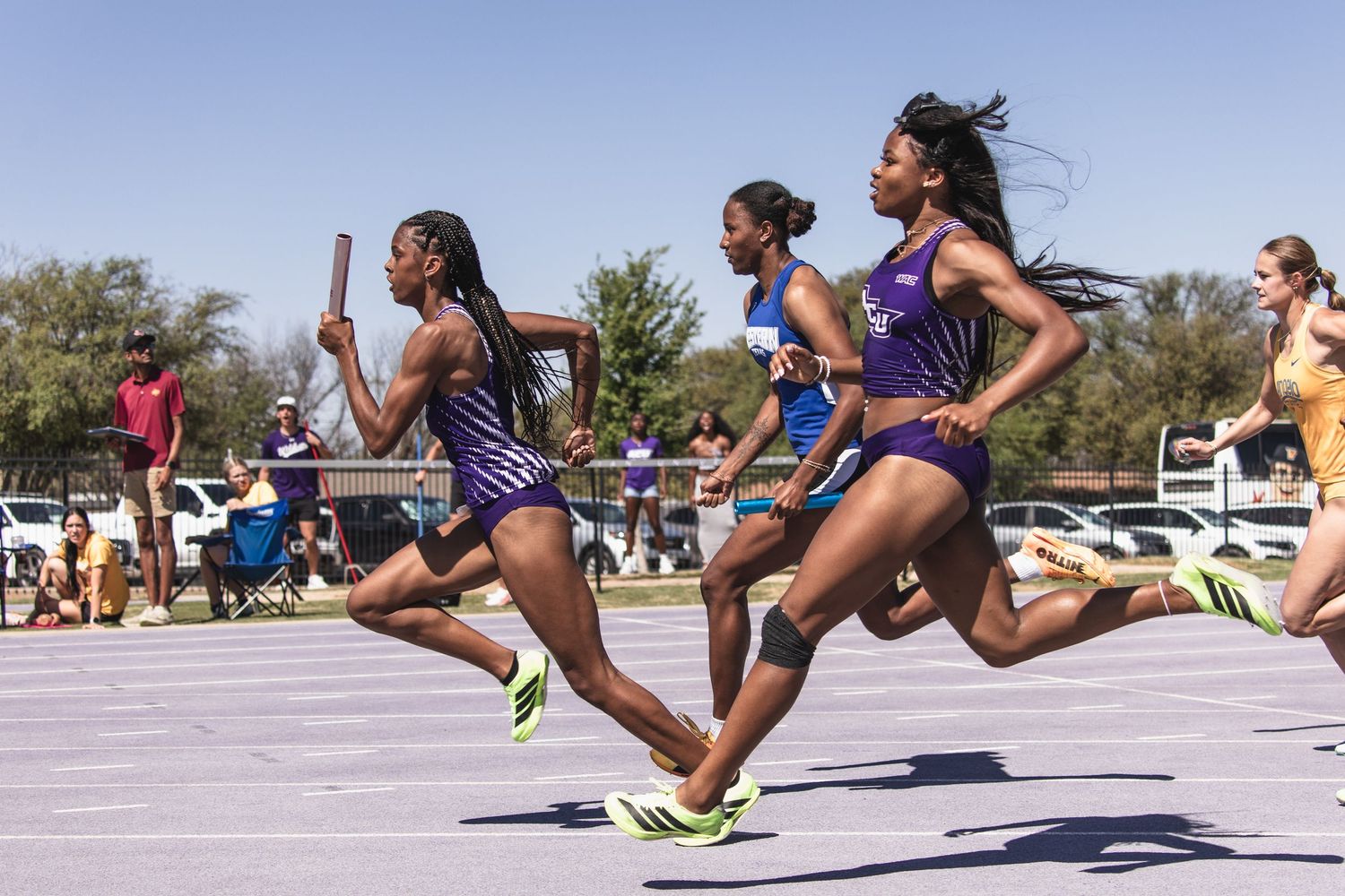 Female ACU relay team passes baton during outdoor track competition.