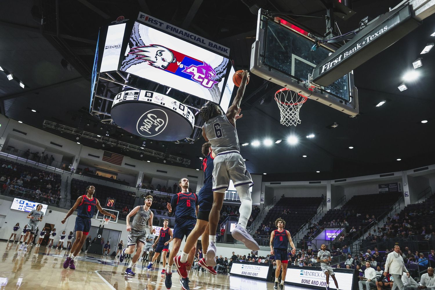 Wide-angle shot of a college basketball player soaring for a dunk in a large indoor arena.