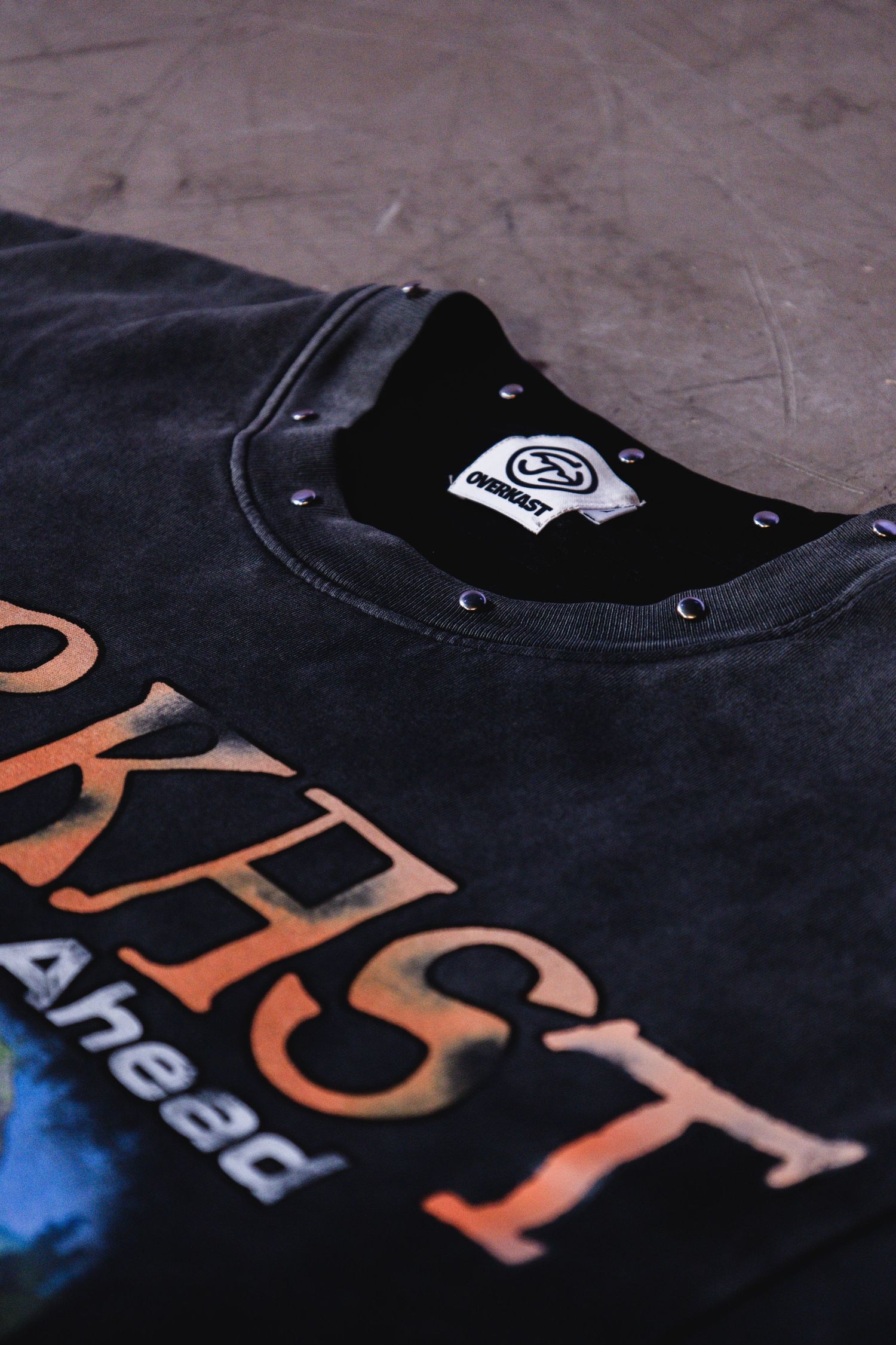 Close-up of a black Overkast branded crewneck sweatshirt with snap buttons and white interior label.