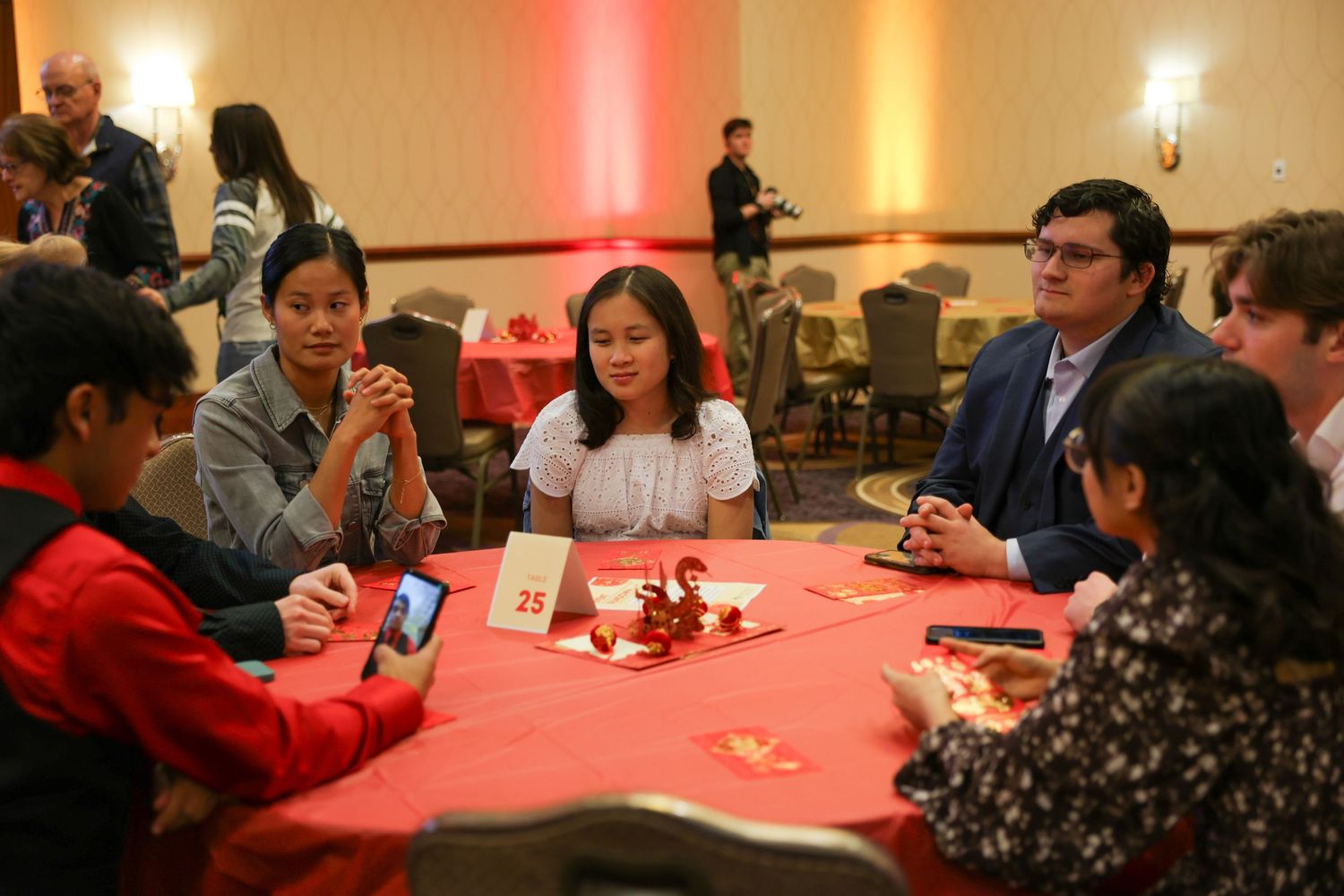Diverse group of guests gather around a red-decorated table at a Chinese New Year celebration event.