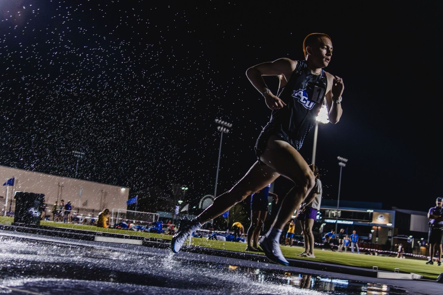 Athlete runs through water obstacle during steeplechase event at night.