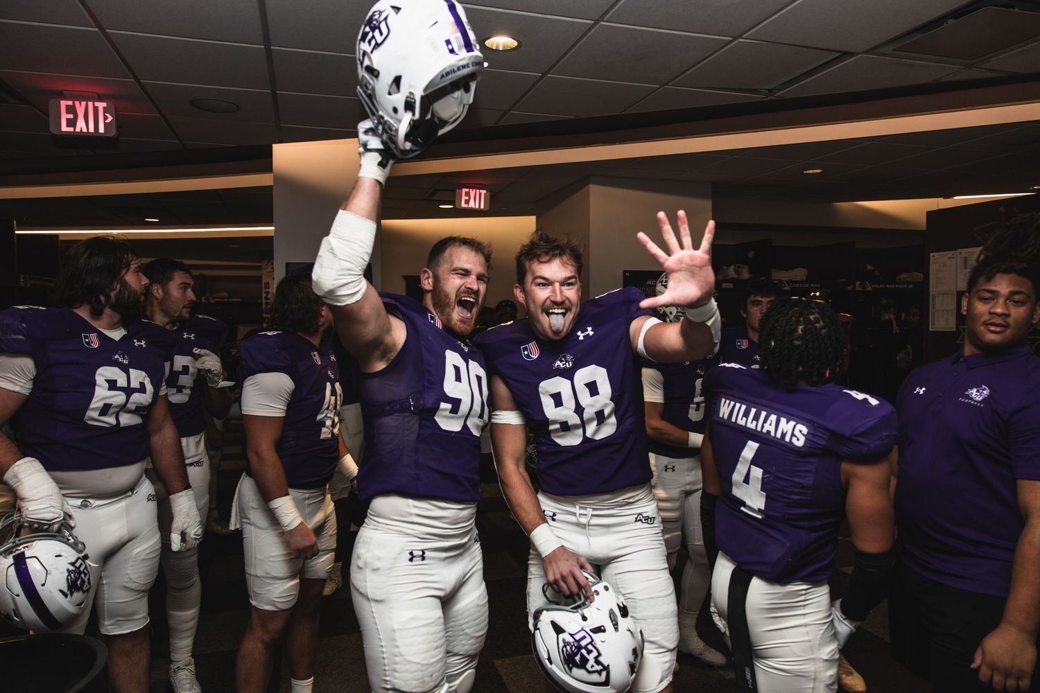 ACU football players #90 and #99 celebrate excitedly in the locker room after a victory.