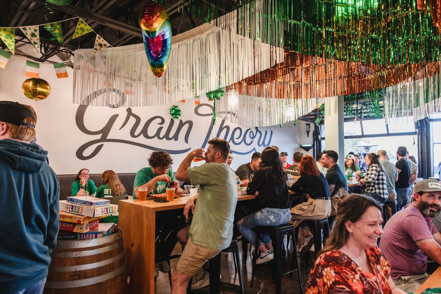 Lively crowd enjoys drinks and socializing inside Grain Theory bar decorated for St. Patricks Day.