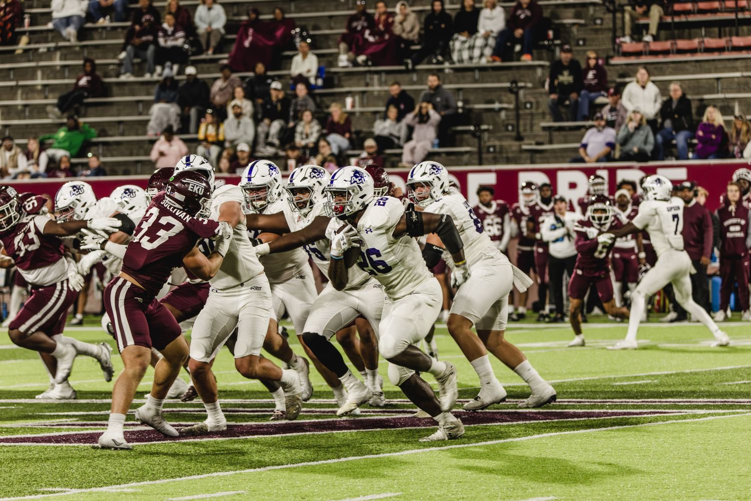 College football players competing in a night game under stadium lights on the field.