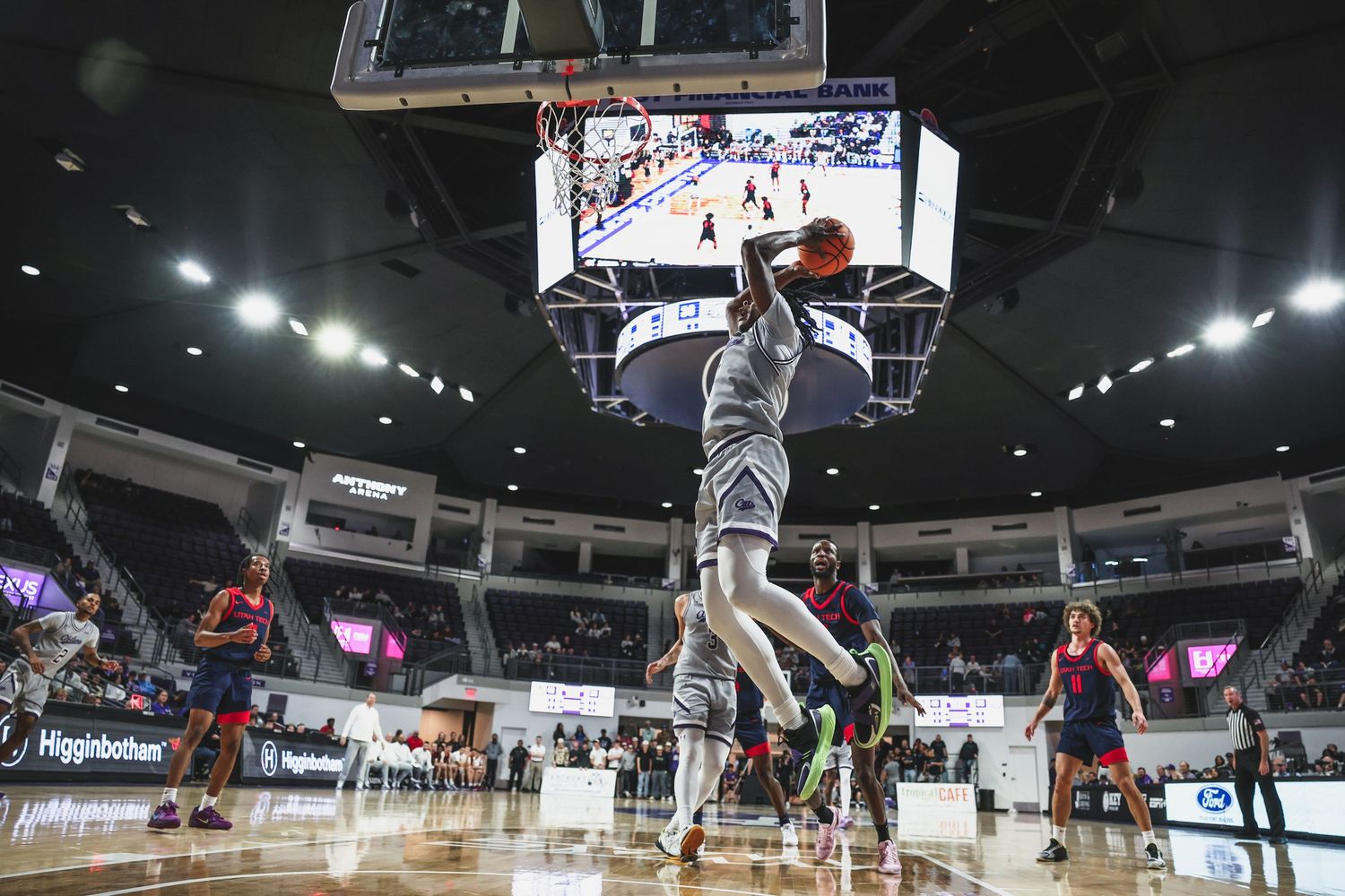 College basketball player executes a powerful dunk in a wide-angle shot showing the full arena court.