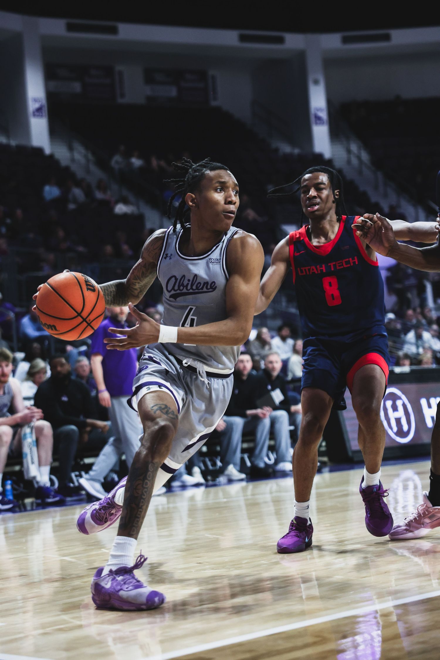 Abilene Christian player number 4 dribbles past Texas Tech number 8 defender during a college basketball game.
