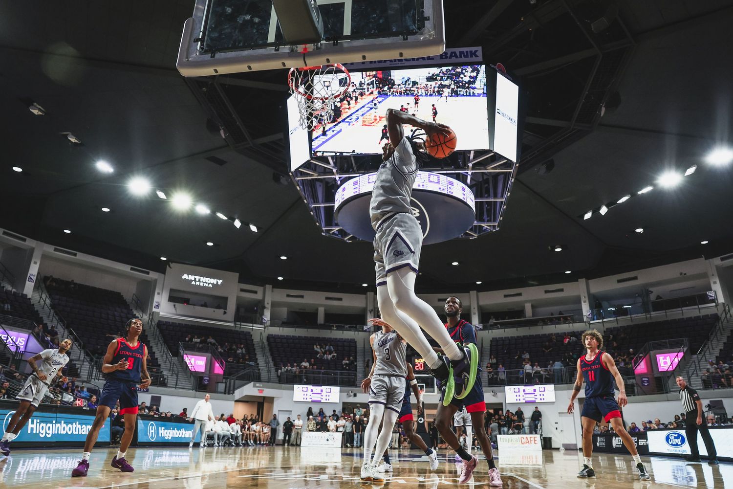 Basketball player soaring for a powerful dunk during a college basketball game in a packed indoor arena.