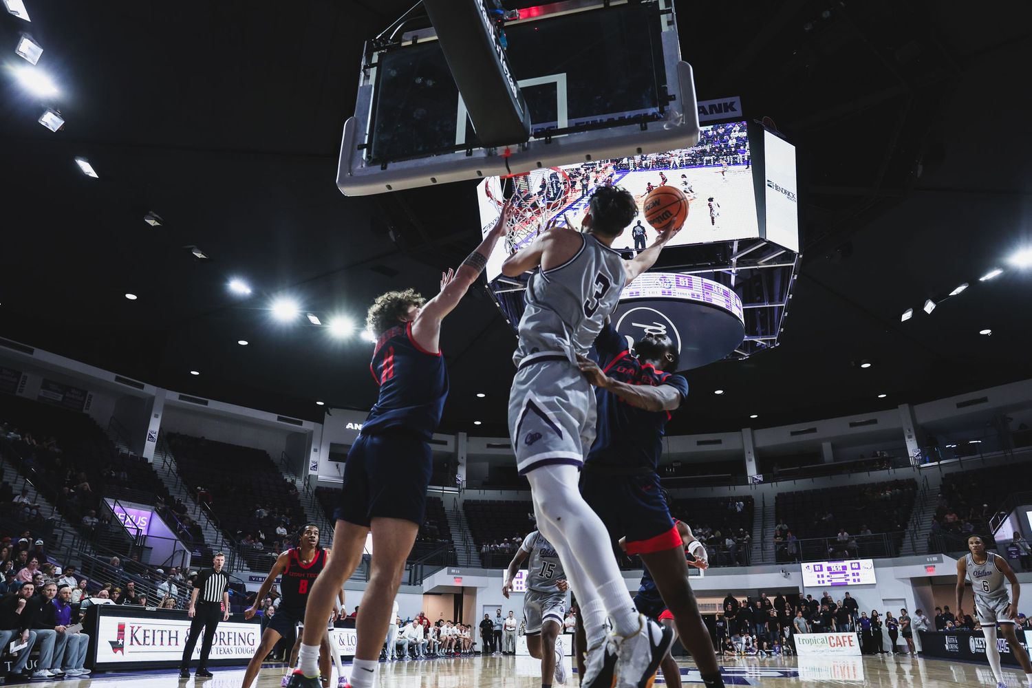 College basketball player attacks the rim for a dunk while a defender attempts to contest the shot.