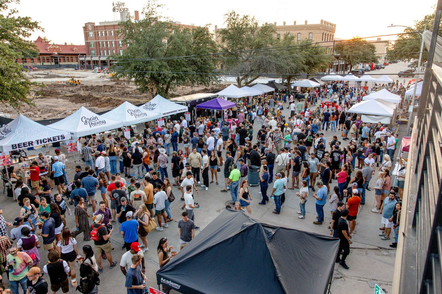 Large crowd gathered at an outdoor festival with white vendor tents at dusk.