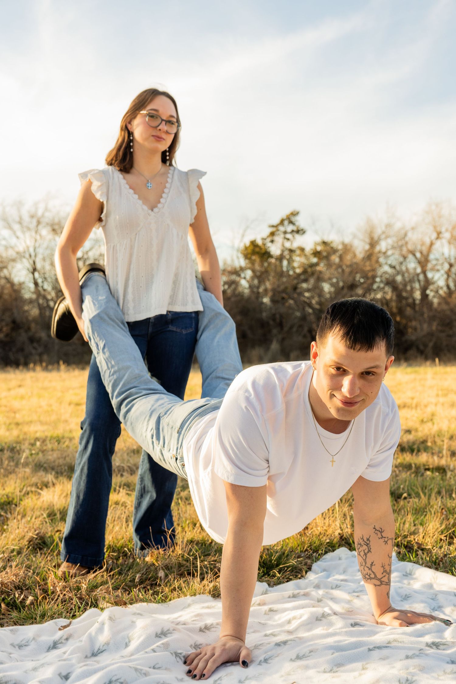Playful couple on a blanket outdoors, woman stepping on mans back as he does a pushup.