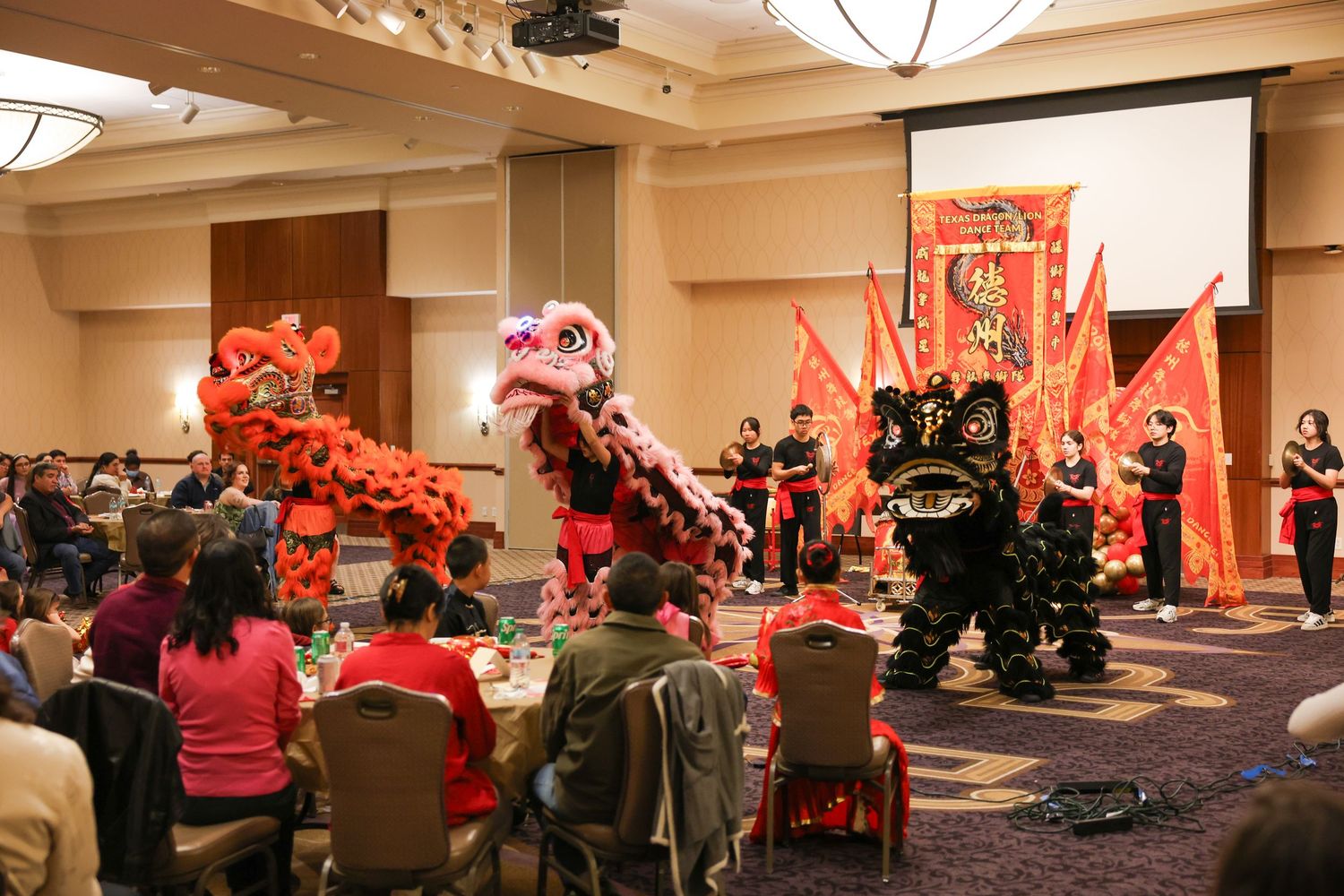 Traditional Chinese lion dancers perform in red and black costumes at a Lunar New Year banquet celebration.