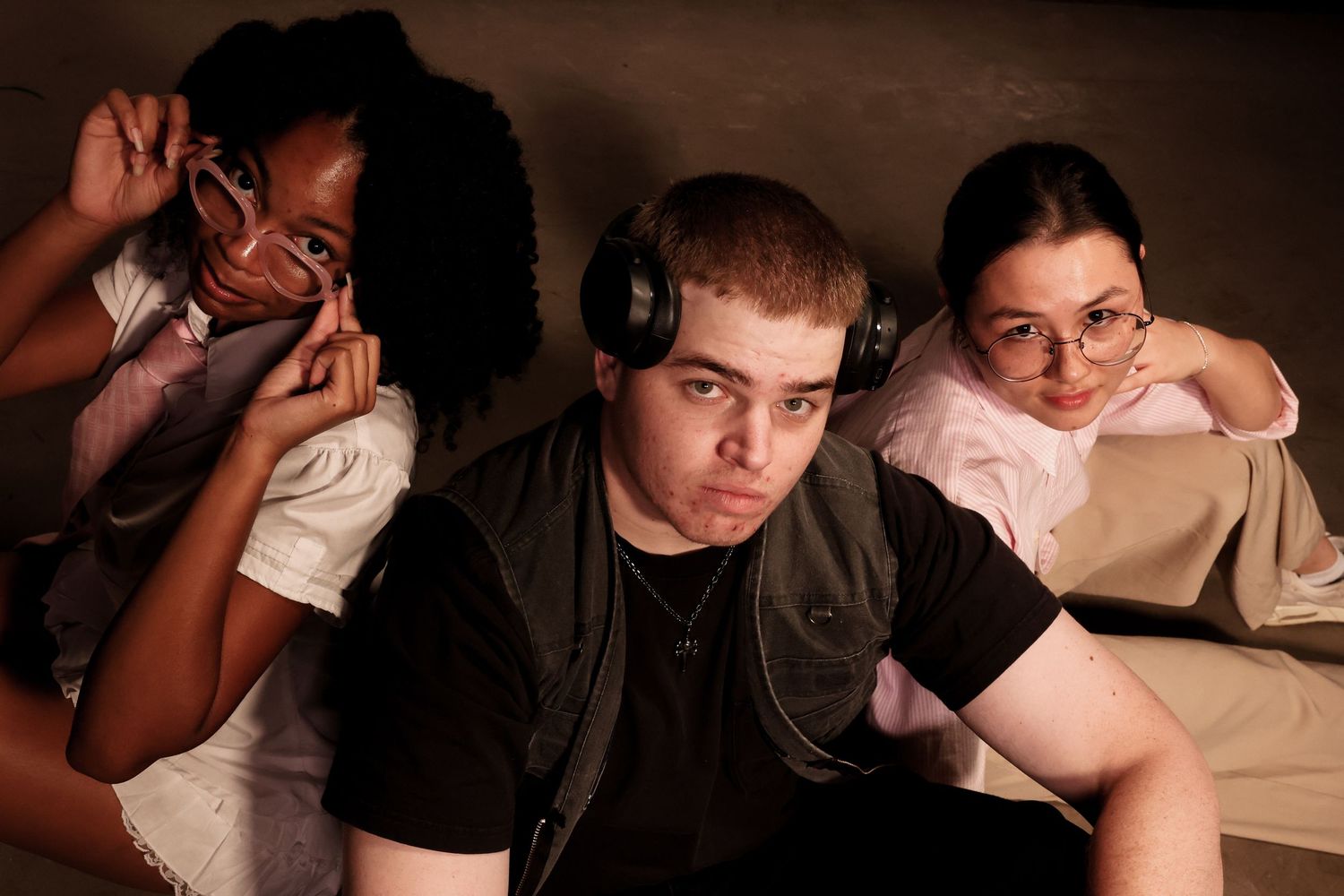 Three young people sitting together, one wearing headphones, posing for a casual indoor photo.