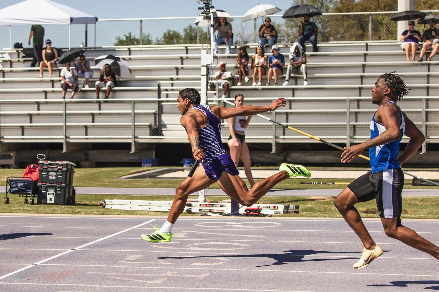 Track athletes compete in relay race baton exchange on outdoor track.