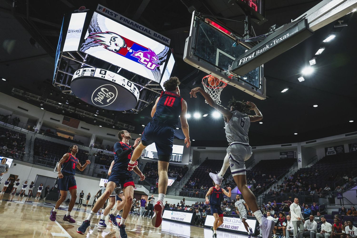 College basketball player throws down a dunk while opponents watch in a large indoor arena.