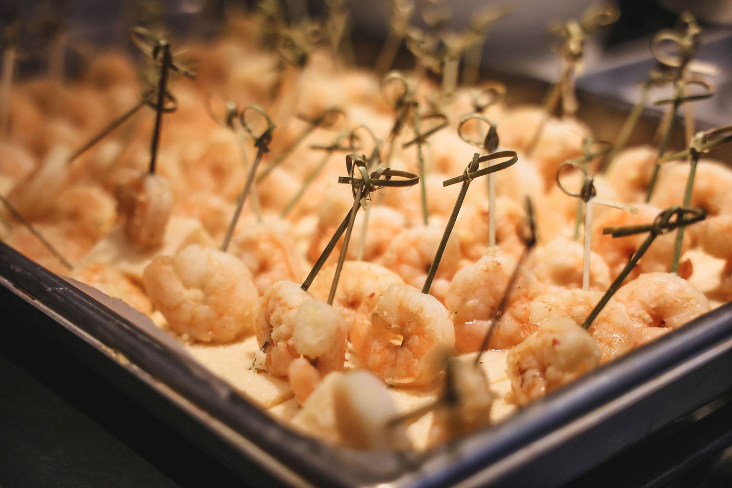 Tray of fresh cooked shrimp appetizers served on toothpick skewers at a catered event.