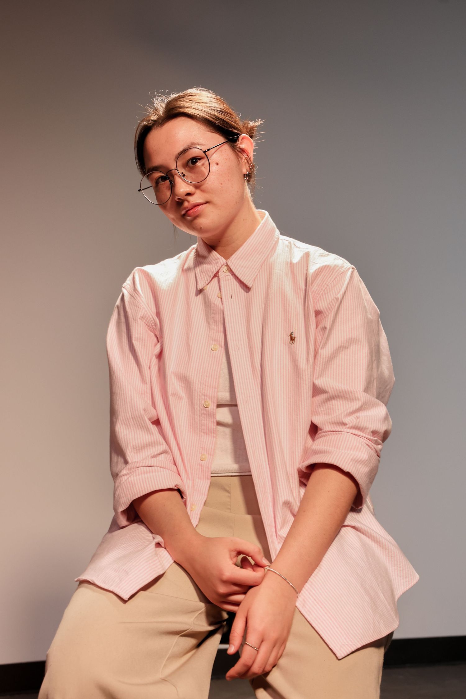 Person in oversized pink Ralph Lauren shirt and glasses sits casually against a gray background.
