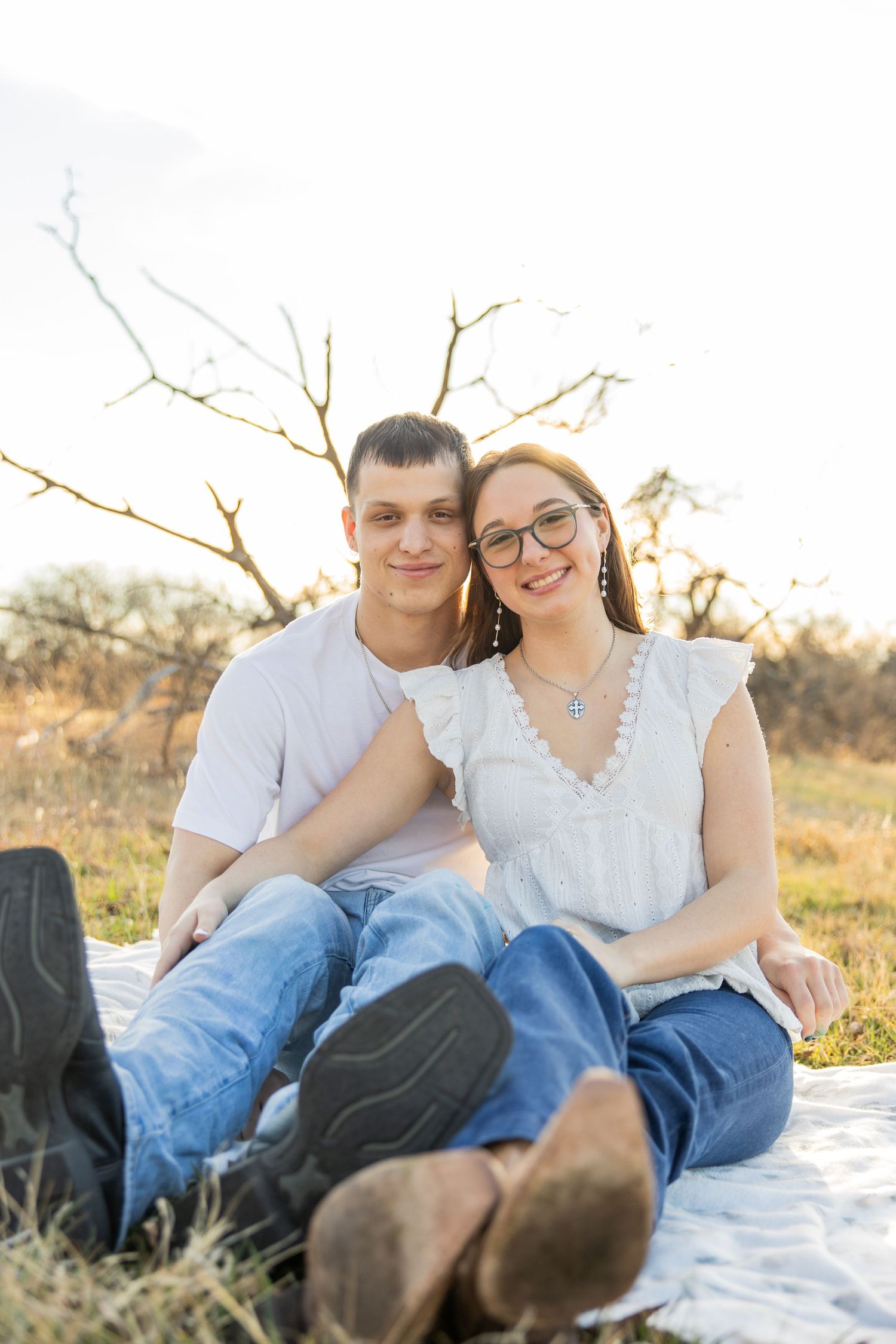 Happy couple sitting together on a blanket in a sunny field, smiling at the camera.