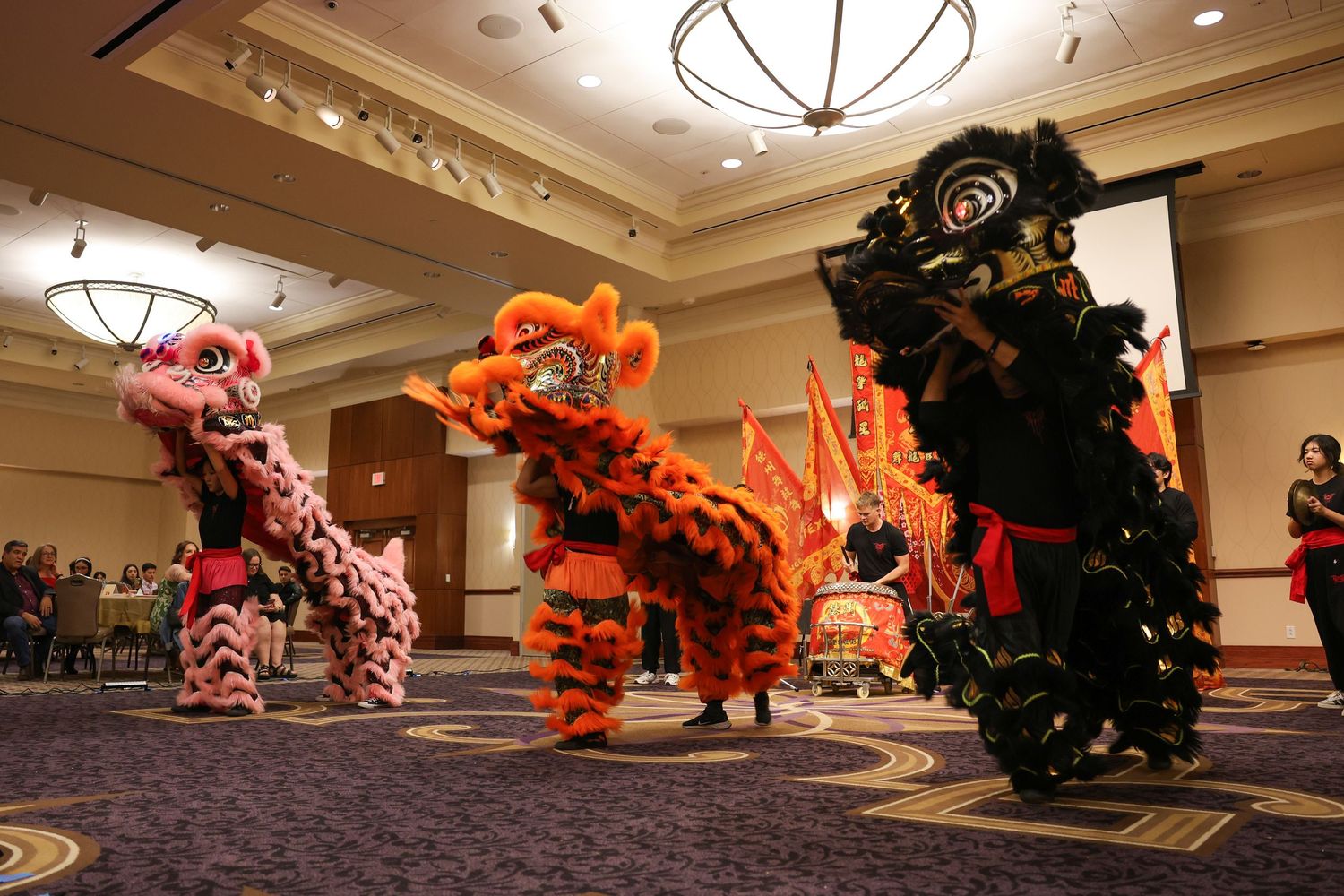Three colorful lion dance costumes performing traditional Chinese New Year celebration in ballroom.