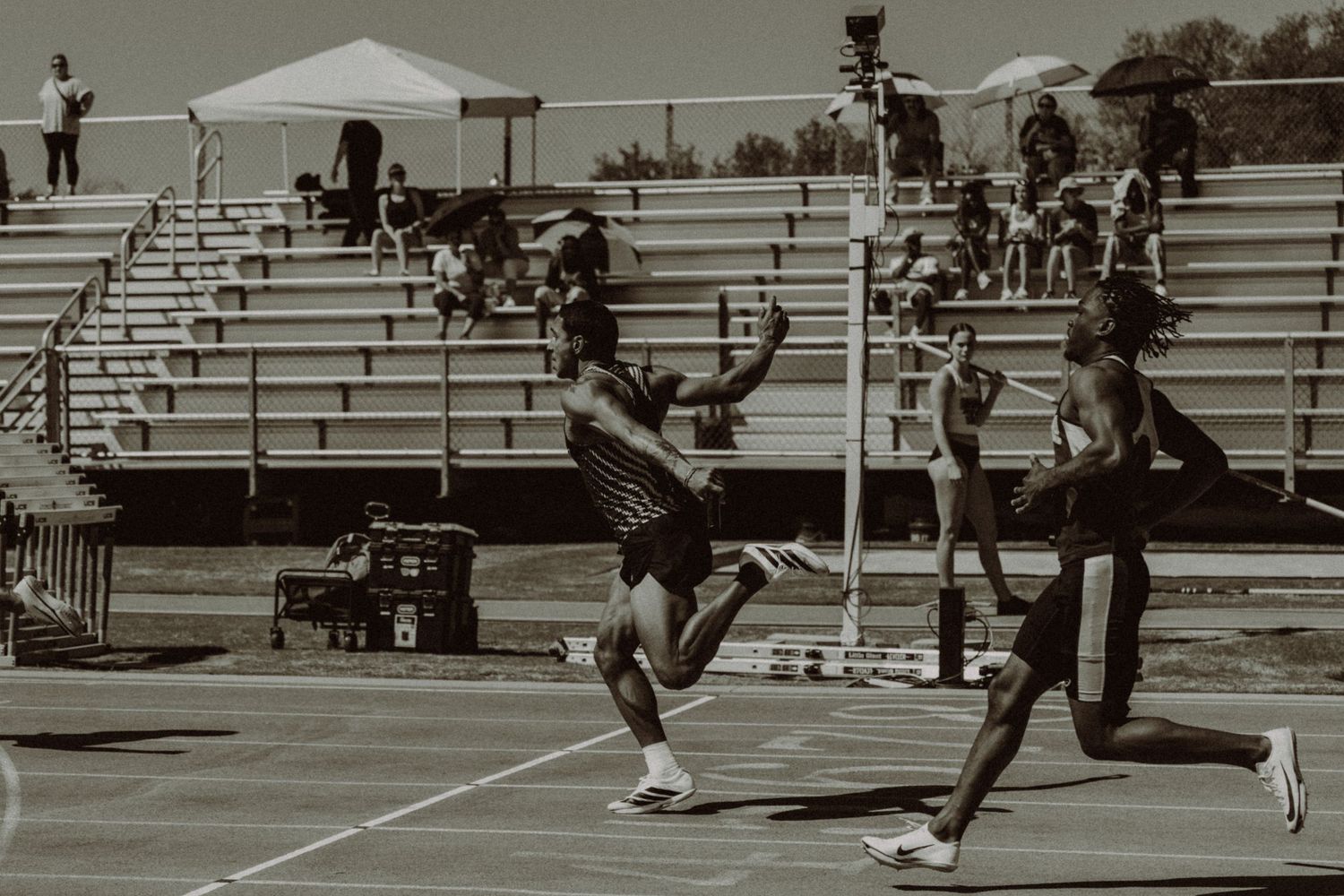 Two athletes compete in relay race handoff on outdoor track, sepia tone.