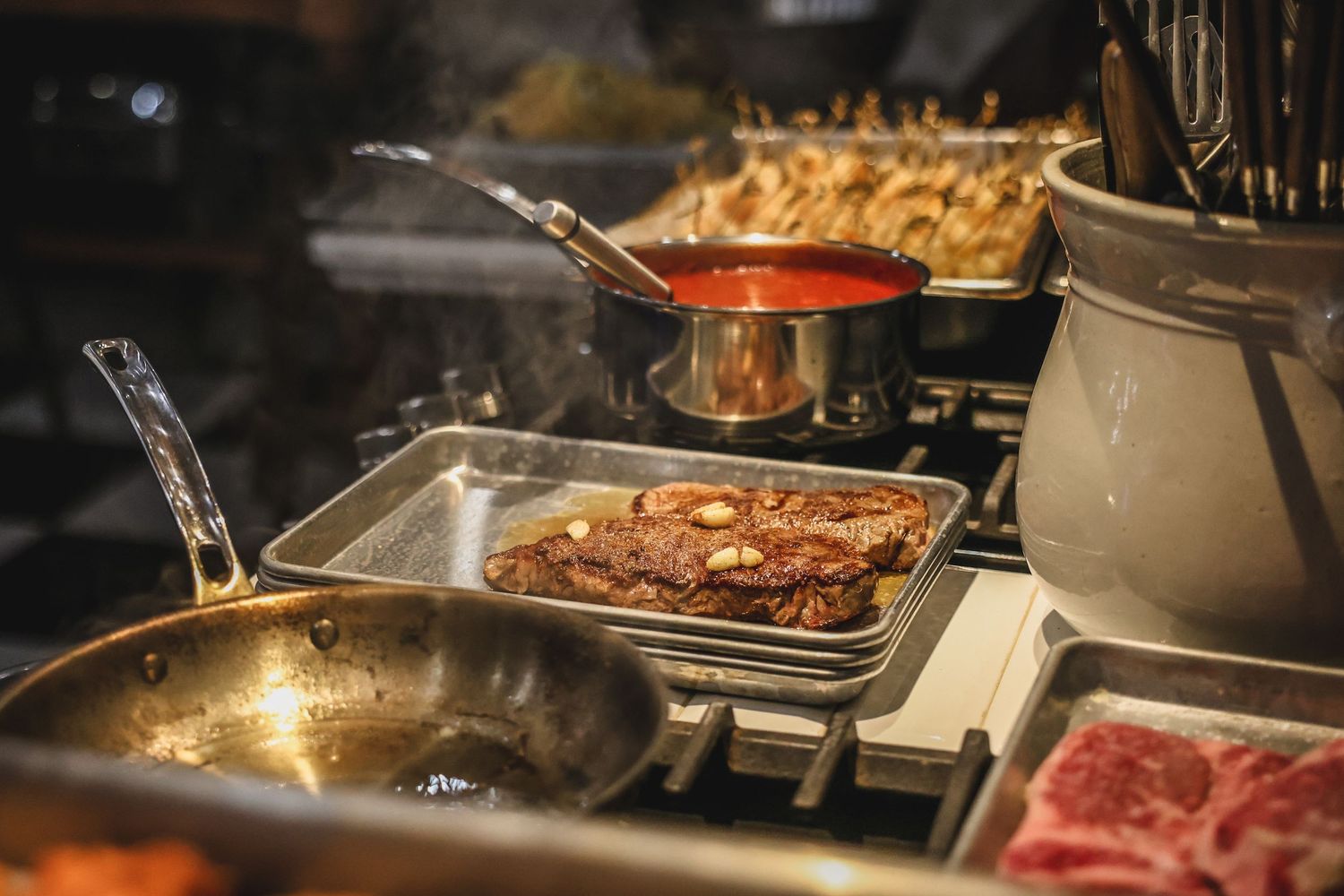 Catering buffet station with grilled steak, red sauce, and skewers under warm kitchen lighting.