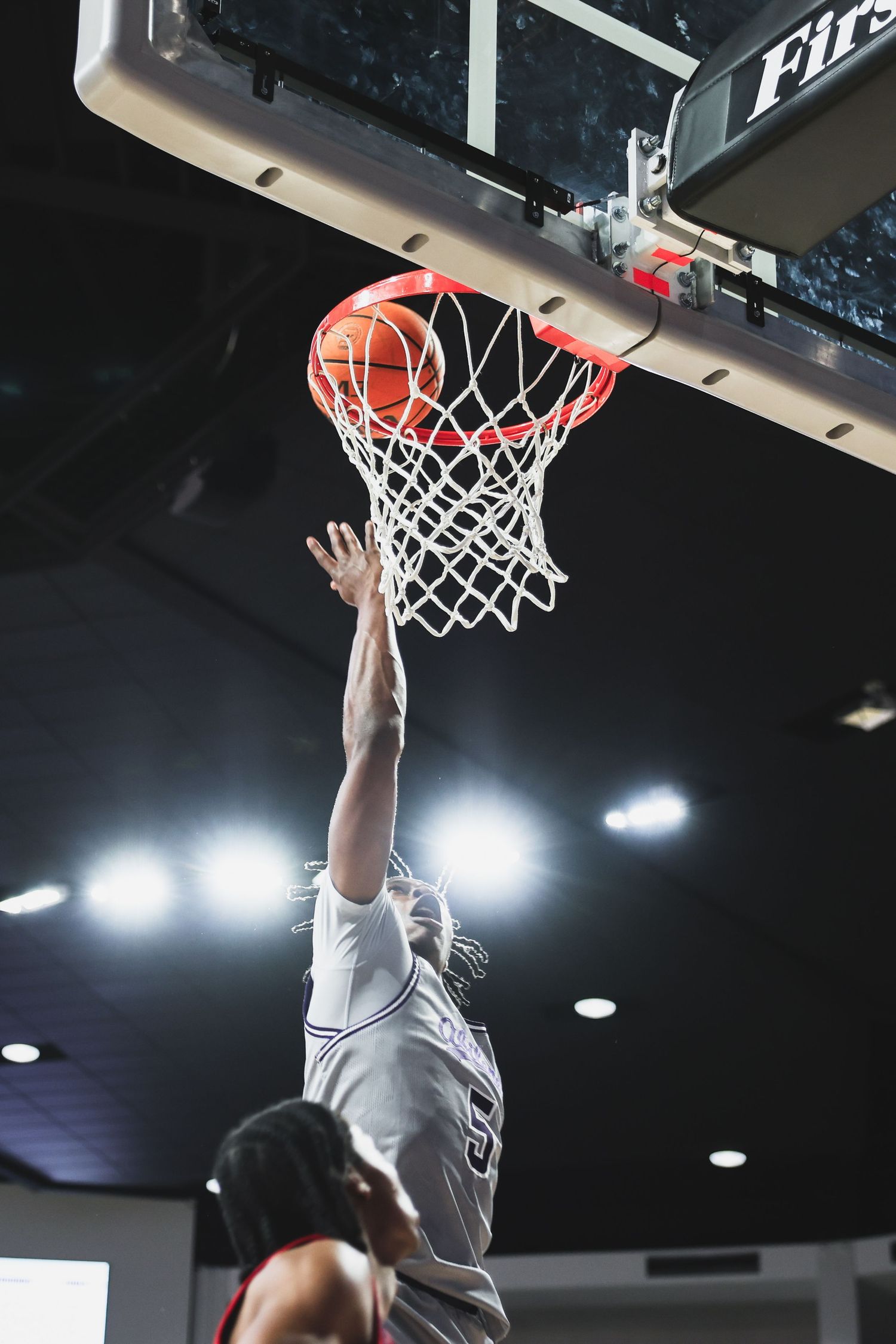 Low-angle view of a basketball player laying the ball up through the hoop during an indoor college game.