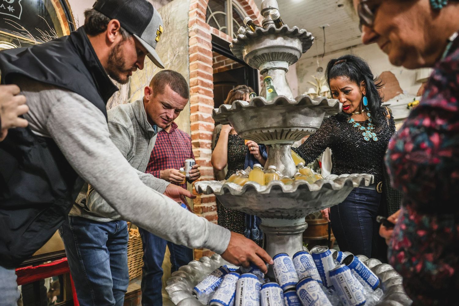 Guests gathered around a stone fountain filled with canned beverages at an indoor event.