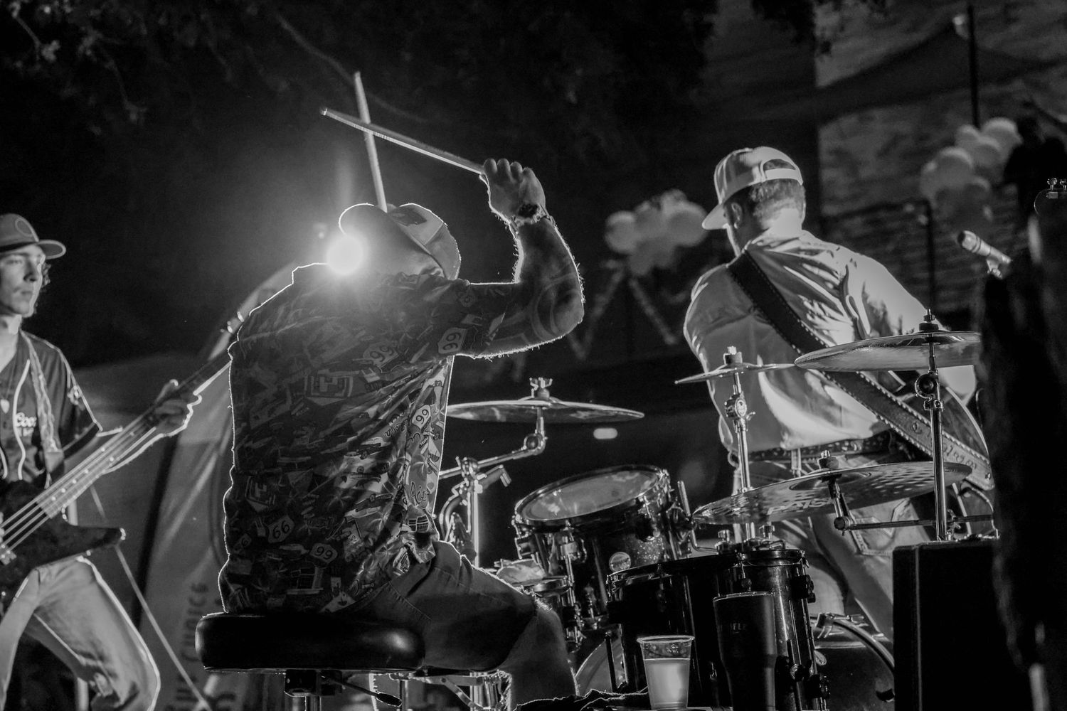 Black and white photo of energetic drummer and guitarist performing at an outdoor nighttime concert.