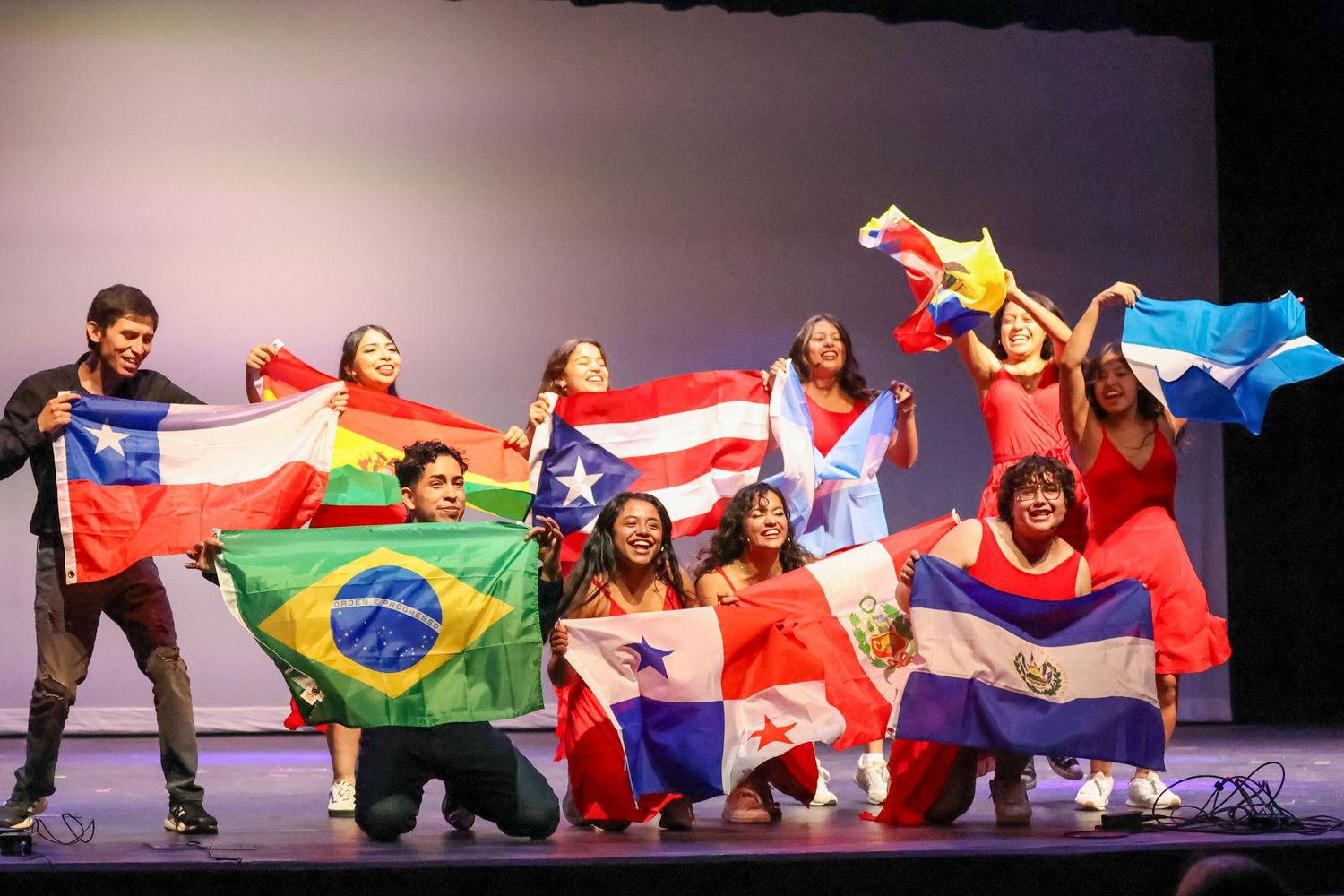 Diverse group of students hold Latin American flags on stage during a multicultural celebration performance.